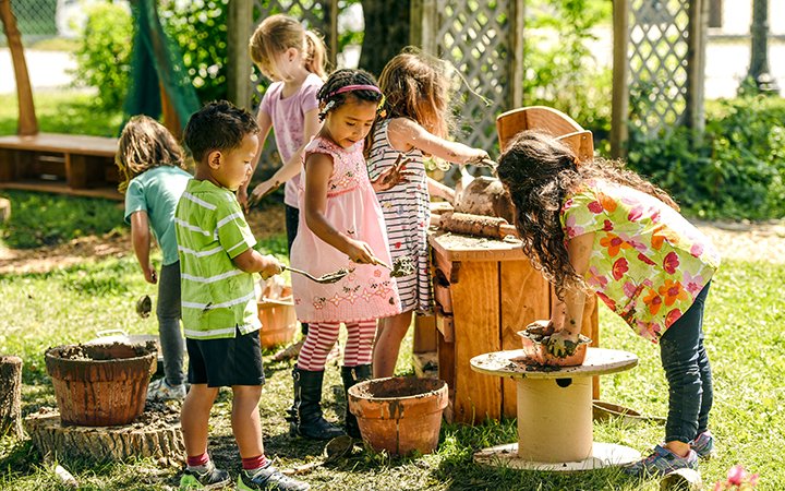 Children playing and working with mud and clay outdoors in a garden, engaging in creative building activities.