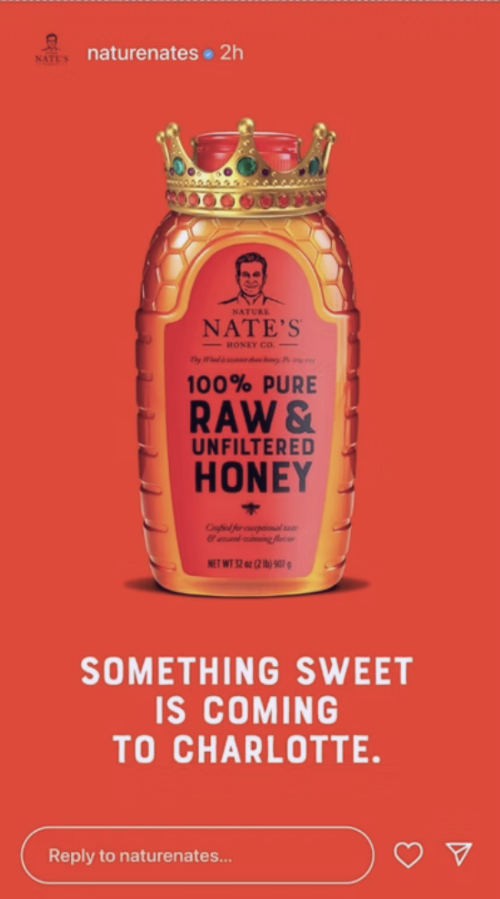 A bottle of Nate's honey, shaped like a honey jar with a crown on top, against a red background. The label indicates it is 100% pure raw and unfiltered honey.