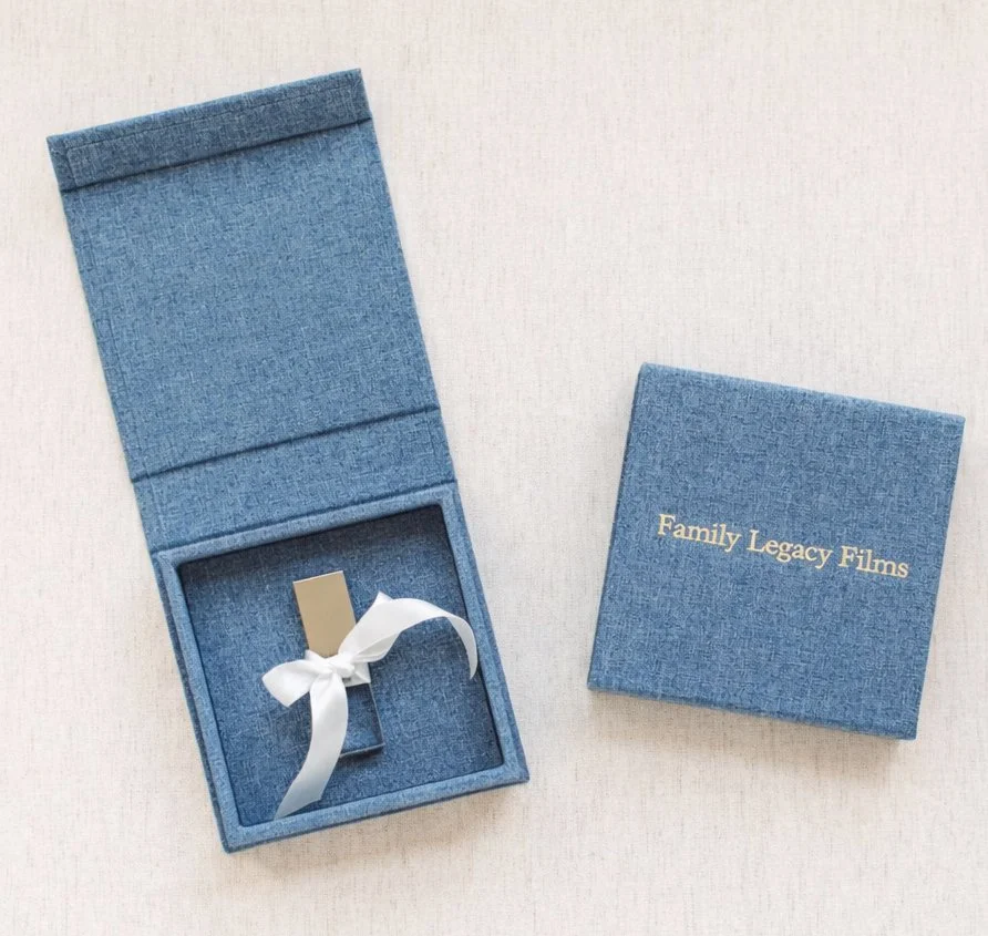 Blue jewelry box with a ribbon inside and a matching blue cover with gold lettering that says 'Family Legacy Films'.