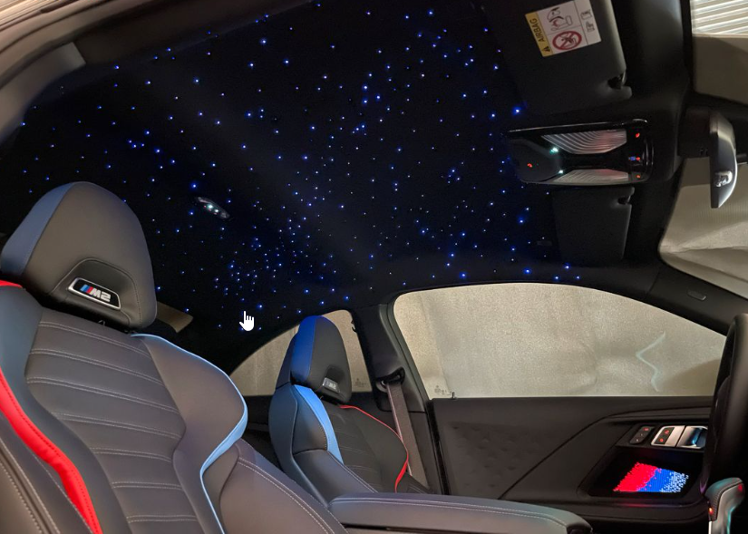 Intérieur d'une voiture avec ciel étoilé LED sur le plafond, sièges en cuir gris avec coutures en rouge et bleu, et tableau de bord moderne.