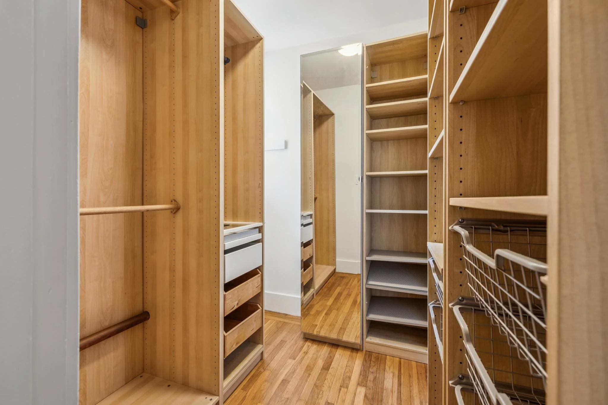 Empty wooden and metal shelving units in a small walk-in closet with hardwood floors.