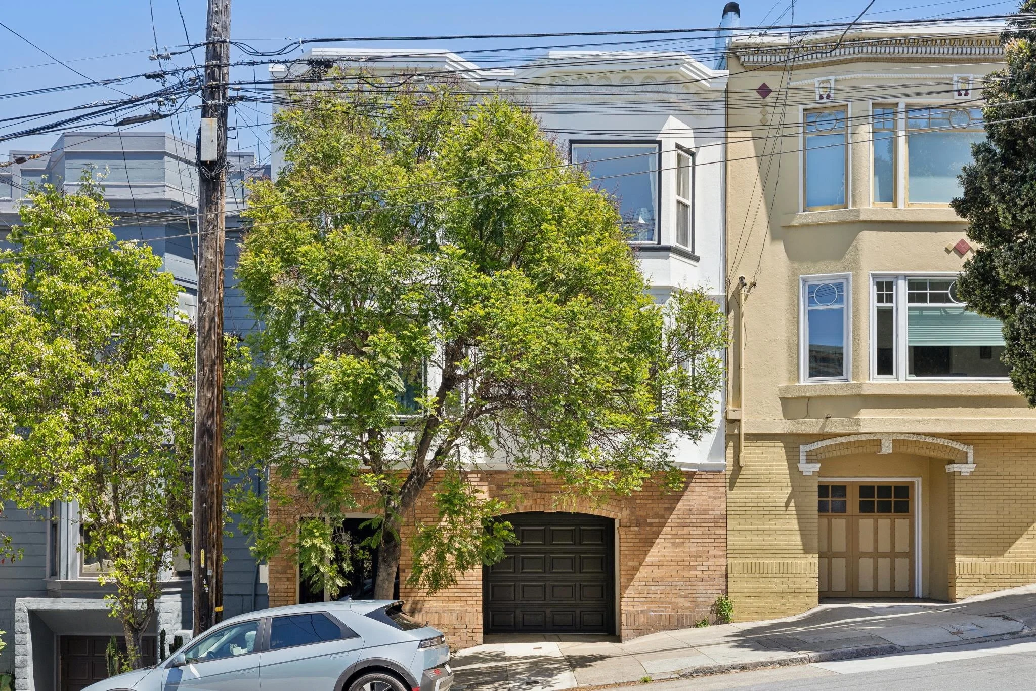 Row of colorful residential houses with tree and car parked in front, power lines overhead, sunny day with clear sky.