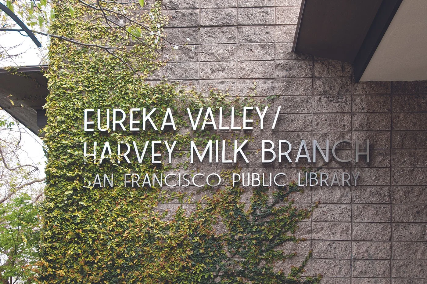 Sign for Eureka Valley Harvey Milk Branch, San Francisco Public Library, mounted on a bricks wall with green foliage.