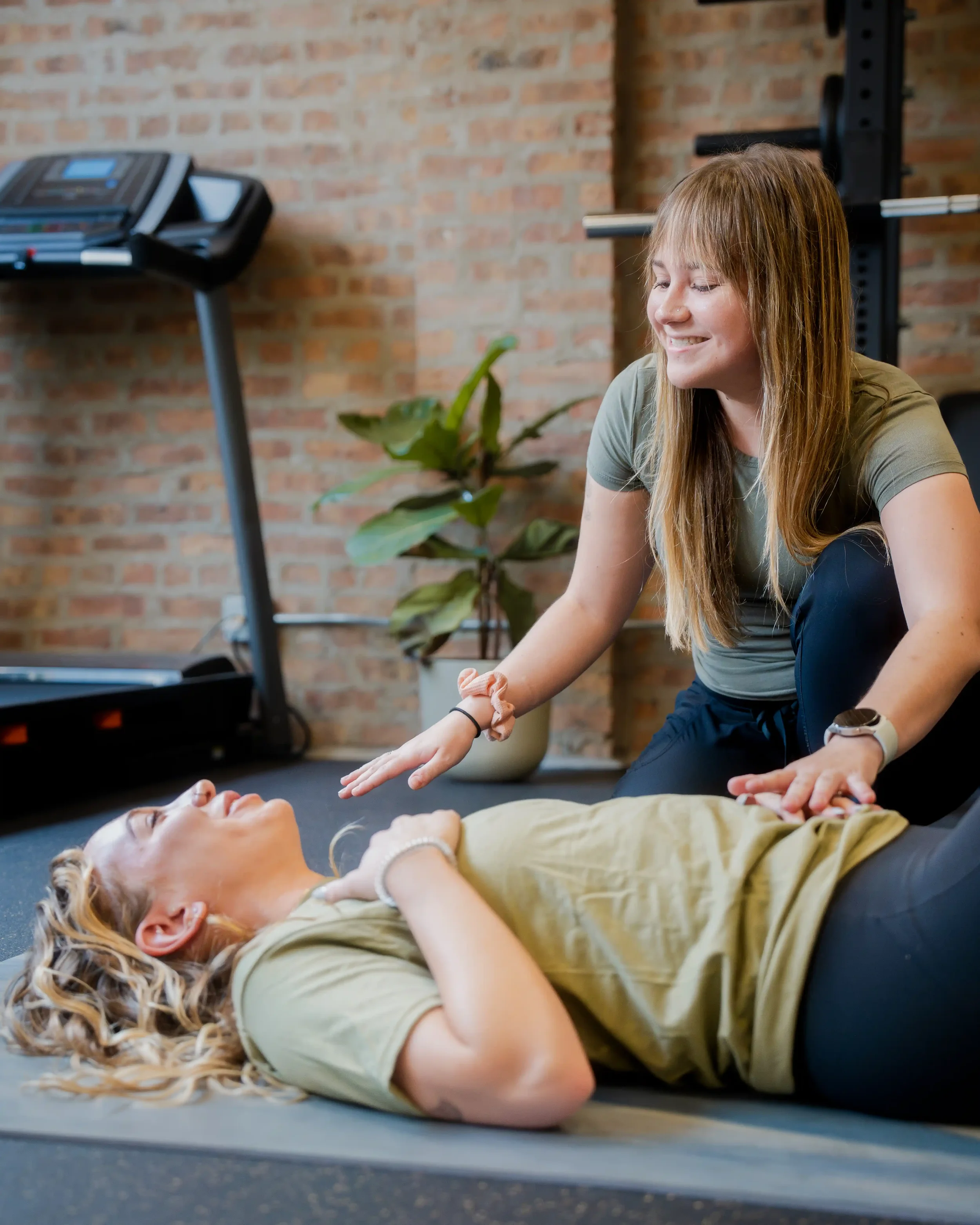 Woman performing CPR on a woman lying on a yoga mat in an indoor gym.