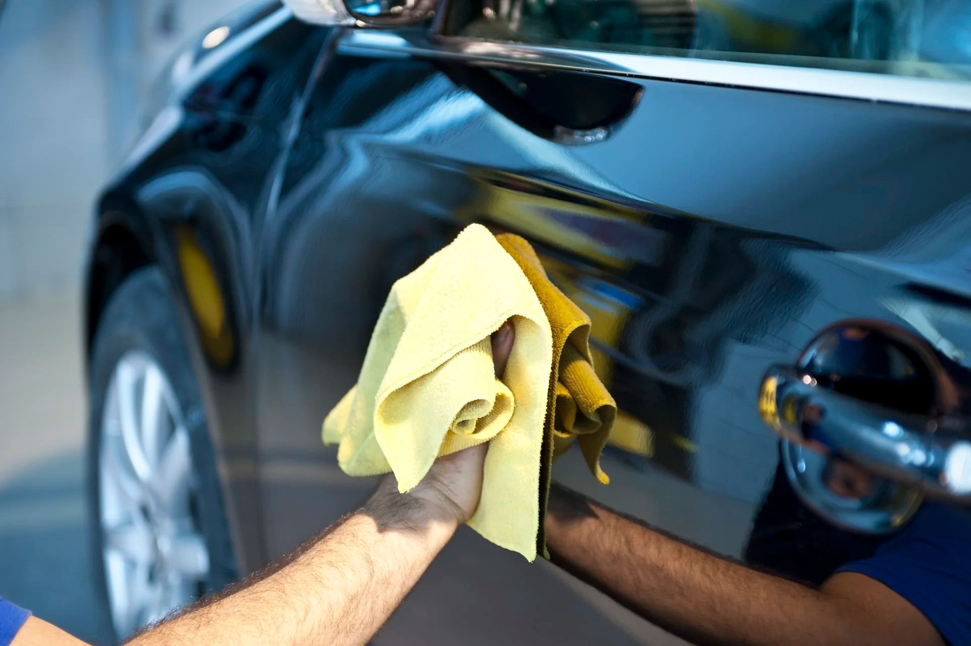 yellow microfibre cloth shinning a black car
