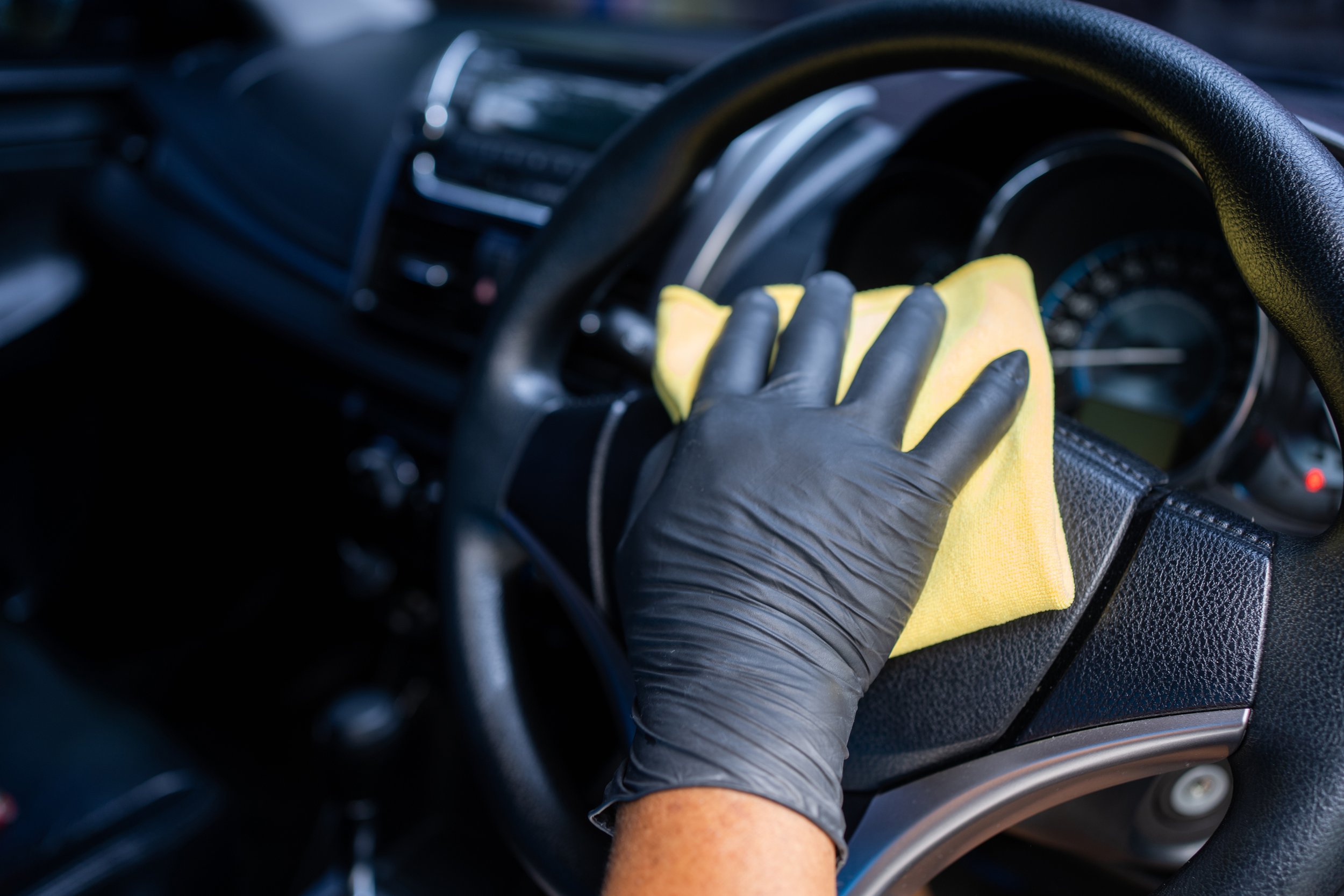 a gloved hand cleaning a steering wheel with yellow microfibre cloth