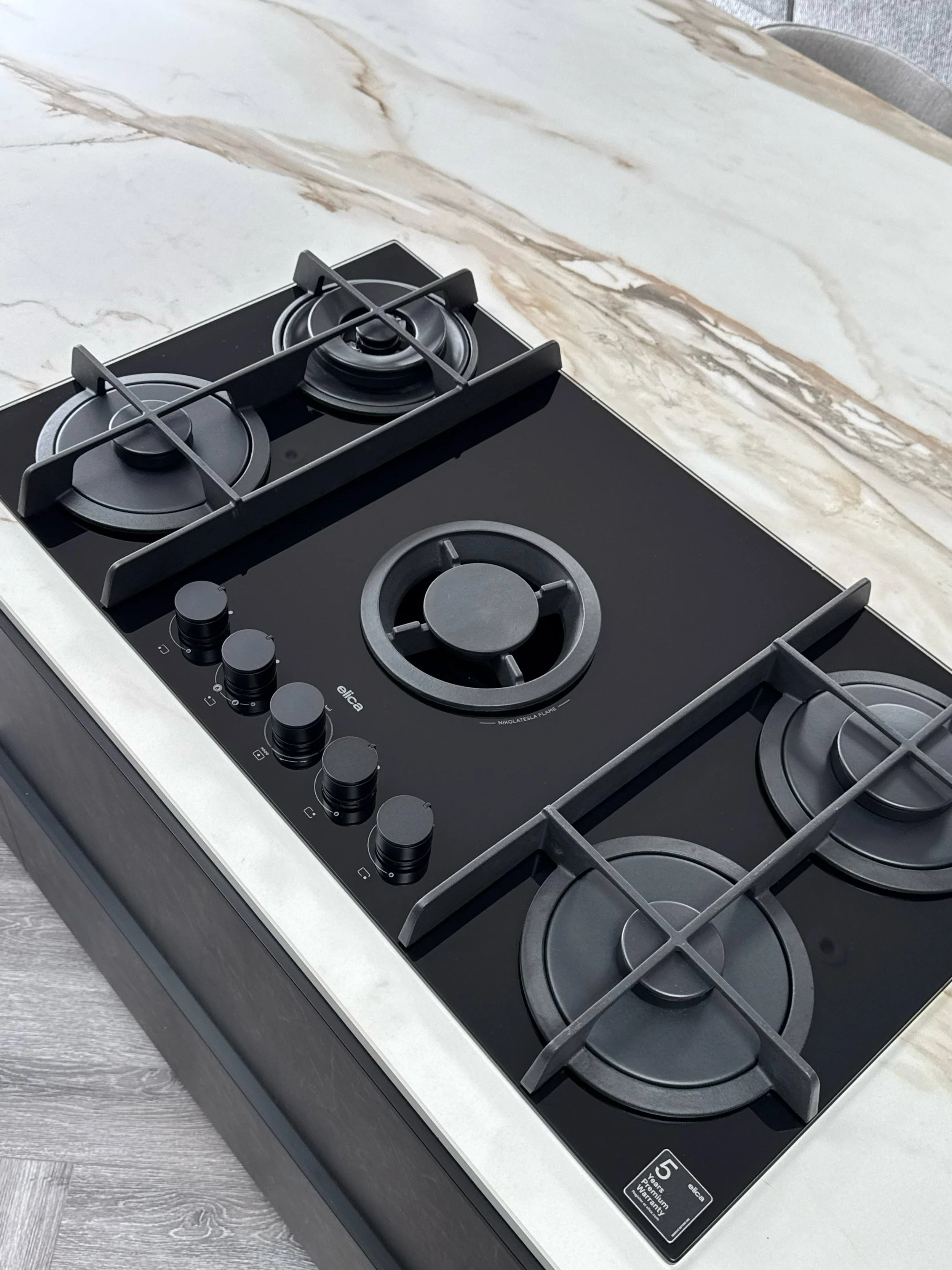 Black gas stove with three burners on a white marble kitchen countertop.