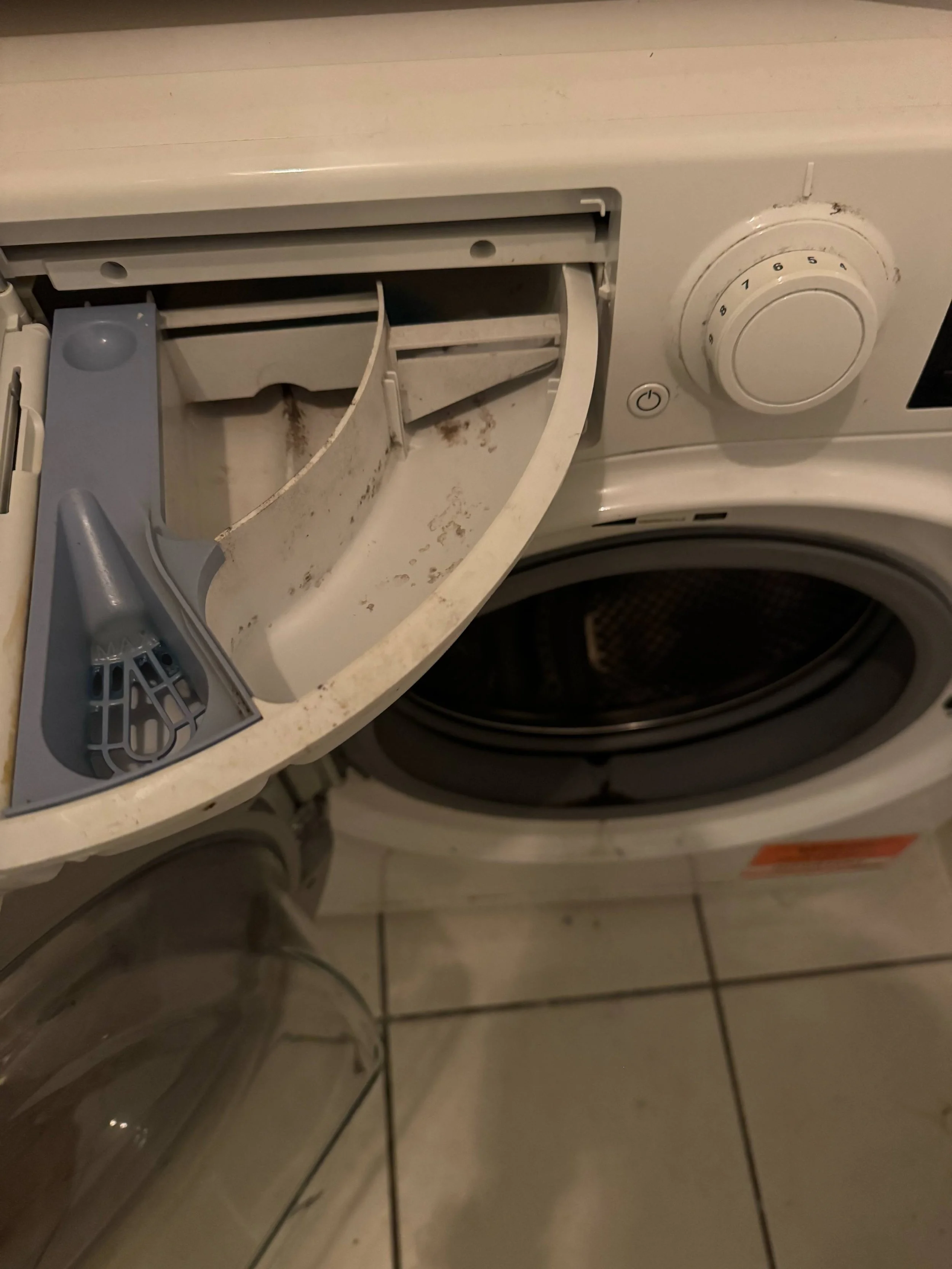 Close-up of a washing machine with the door open, showing dirt and mold inside.