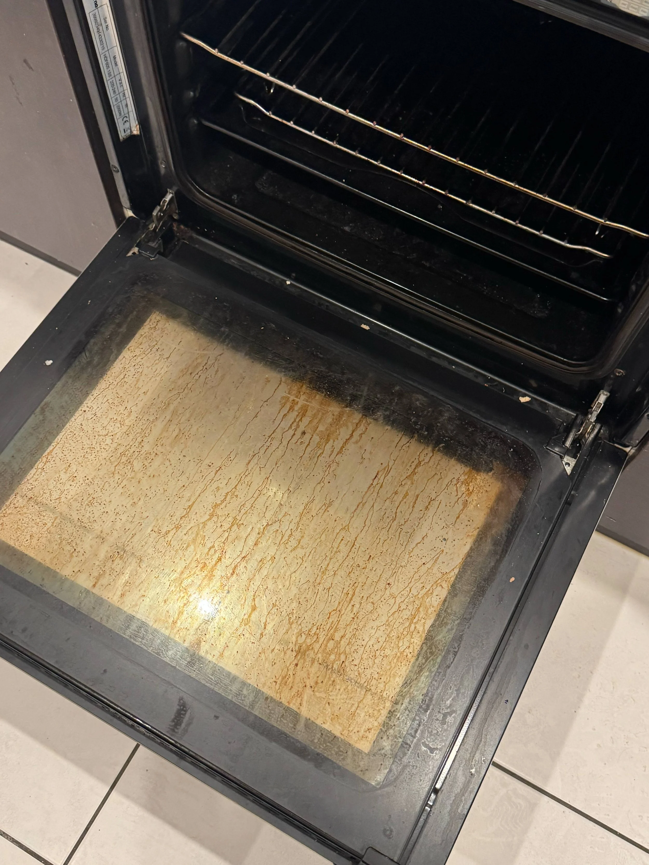 Empty oven with baked-on grime and a parchment paper liner on the baking sheet.