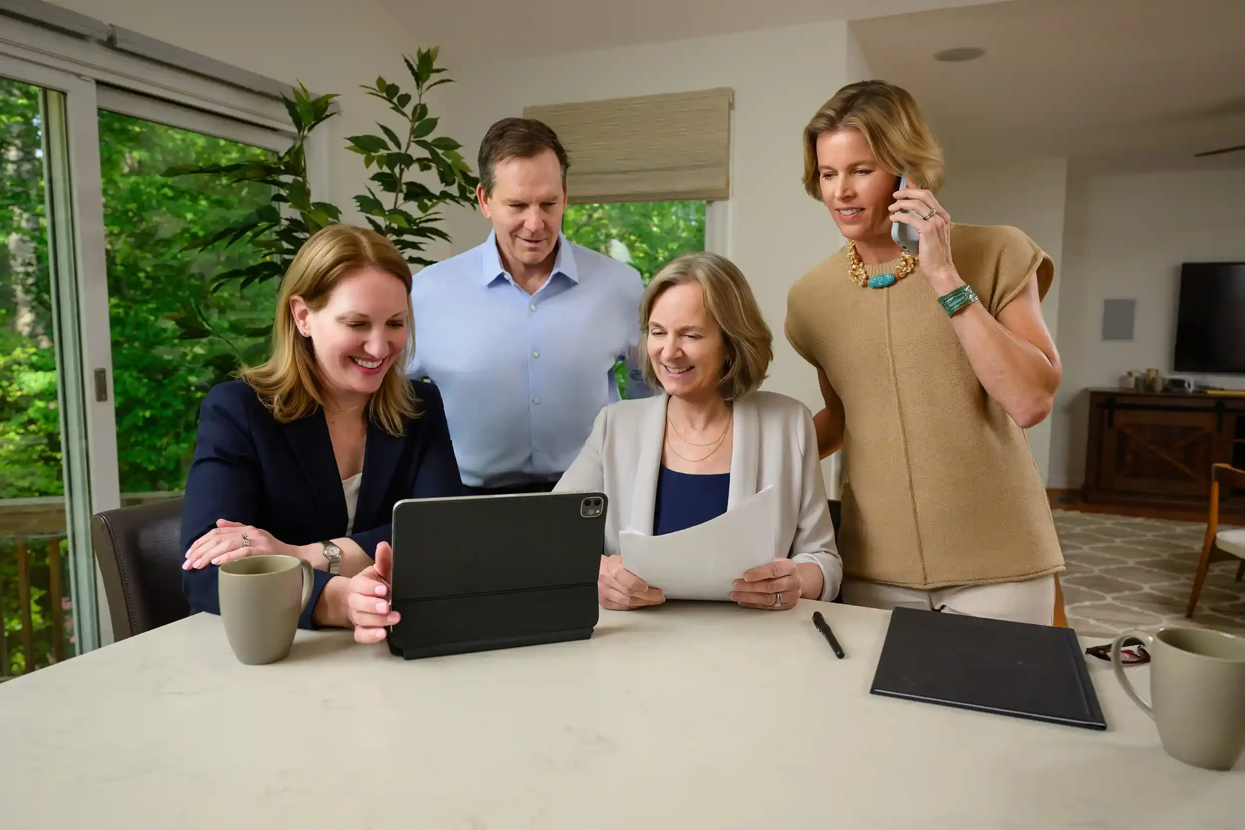 The Beall & Rehill team gathered around a laptop during a meeting or discussion inside a house with large windows and green outdoor scenery