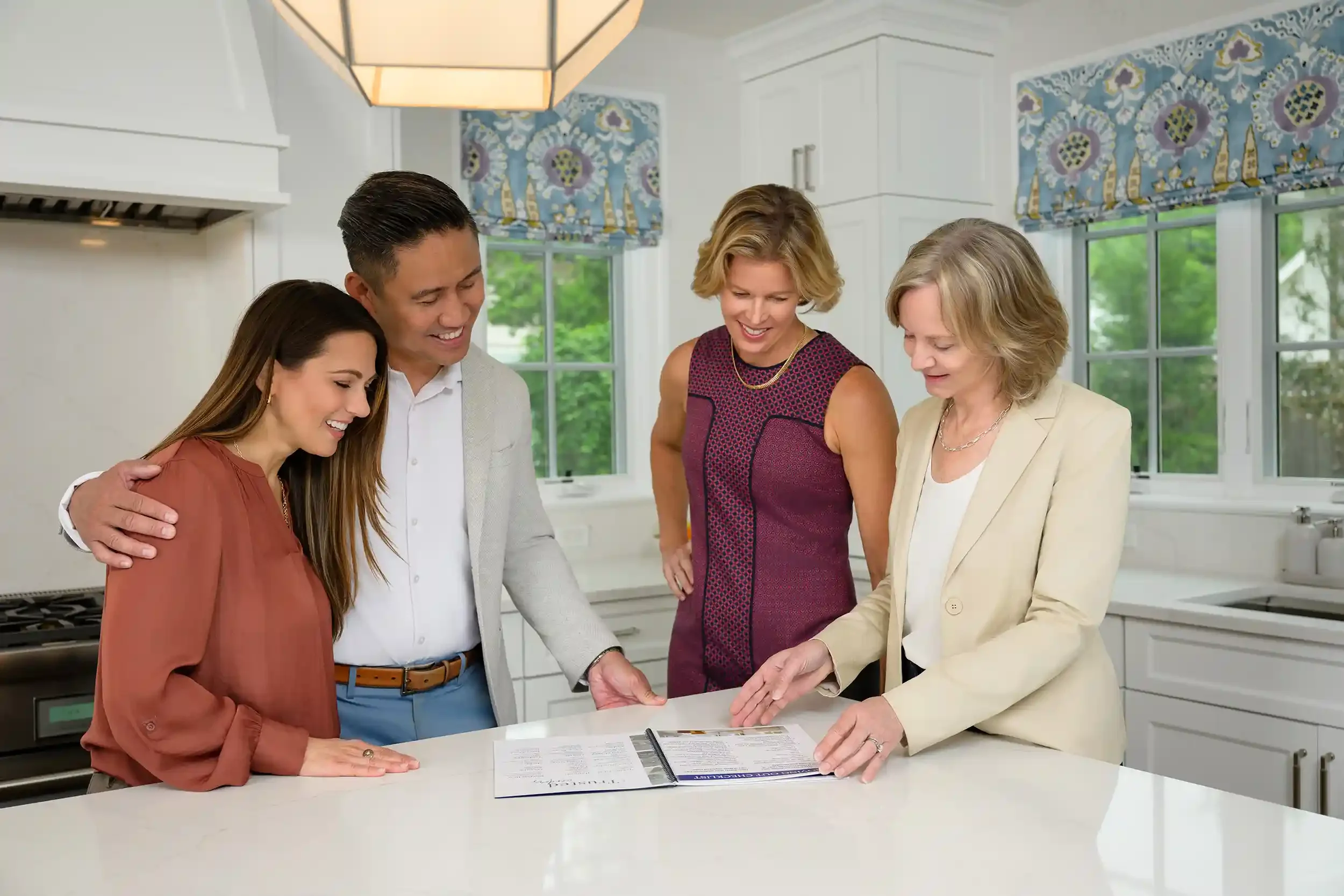 Alex Beall, Kathy Rehill, and clients gather around a kitchen island looking at a document