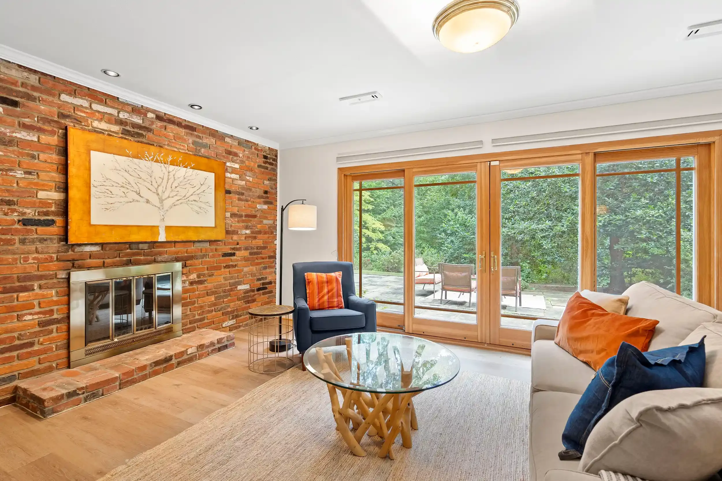Living room with brick fireplace, large window, and outdoor patio with chairs.