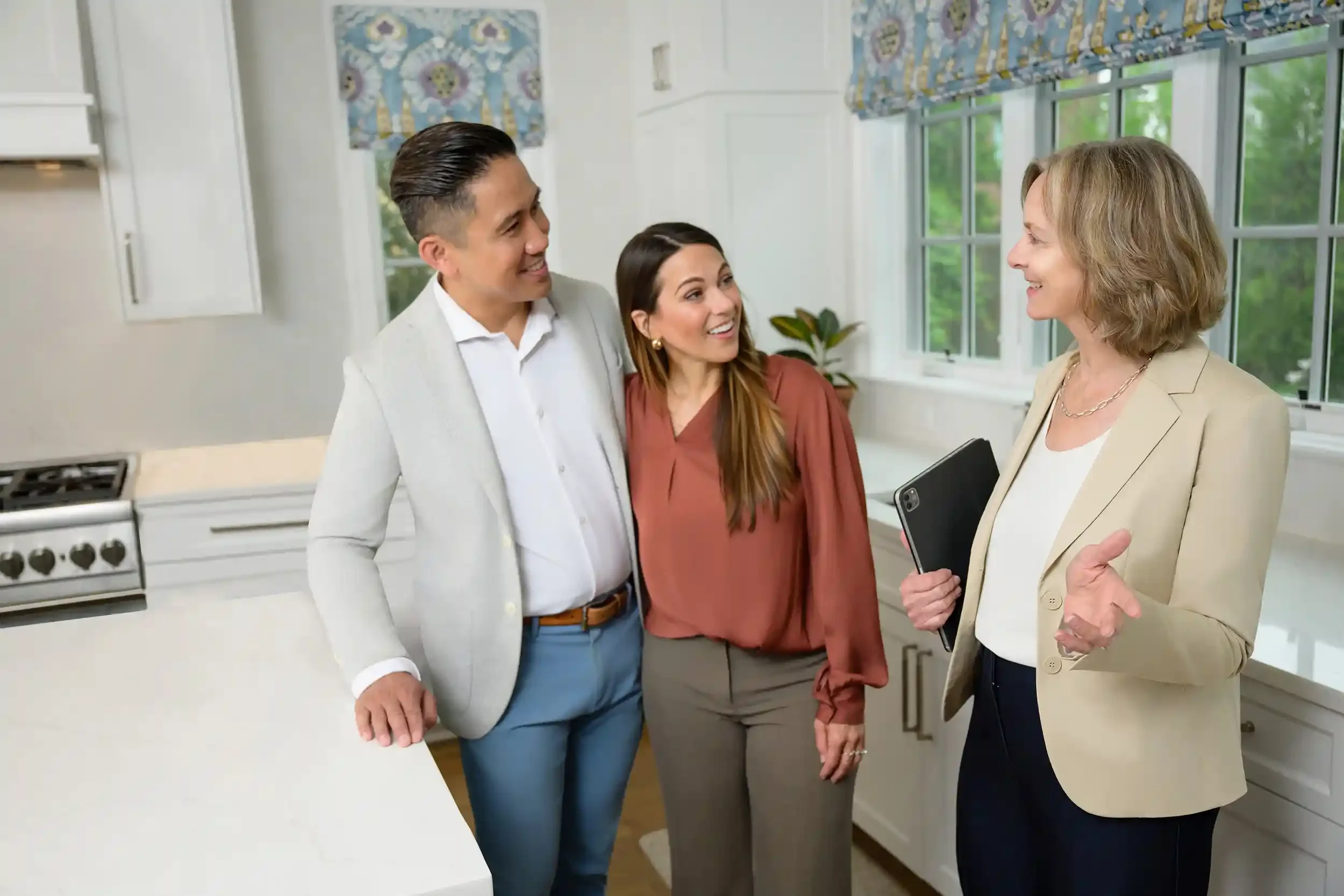 Kathy Rehill having a conversation with clients in a kitchen with large windows, white cabinets, and a stove