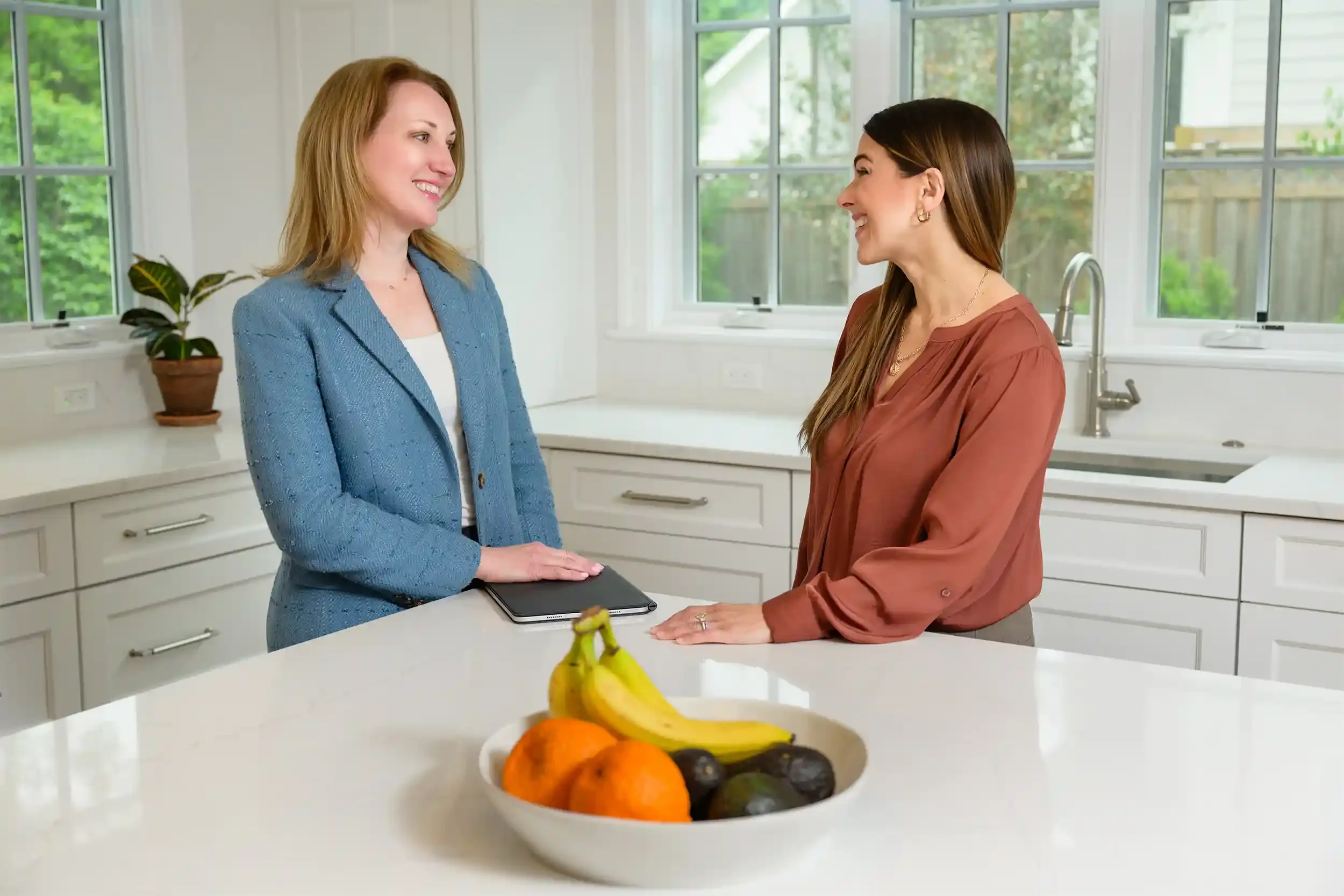 Allison Rivera and the client are smiling and talking in a bright kitchen with large windows