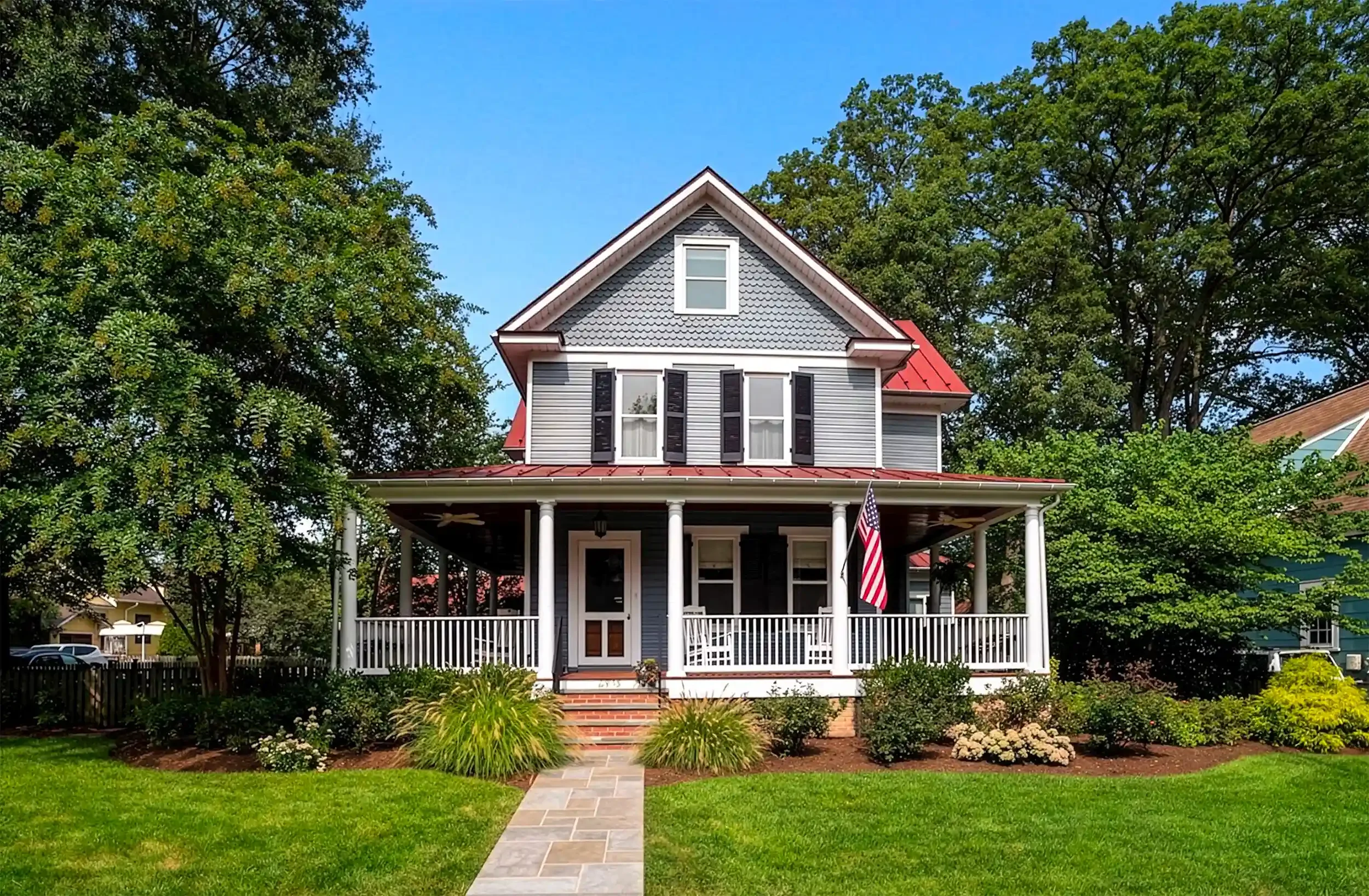 A two-story house with a gray exterior, black shutters, and a red metal roof