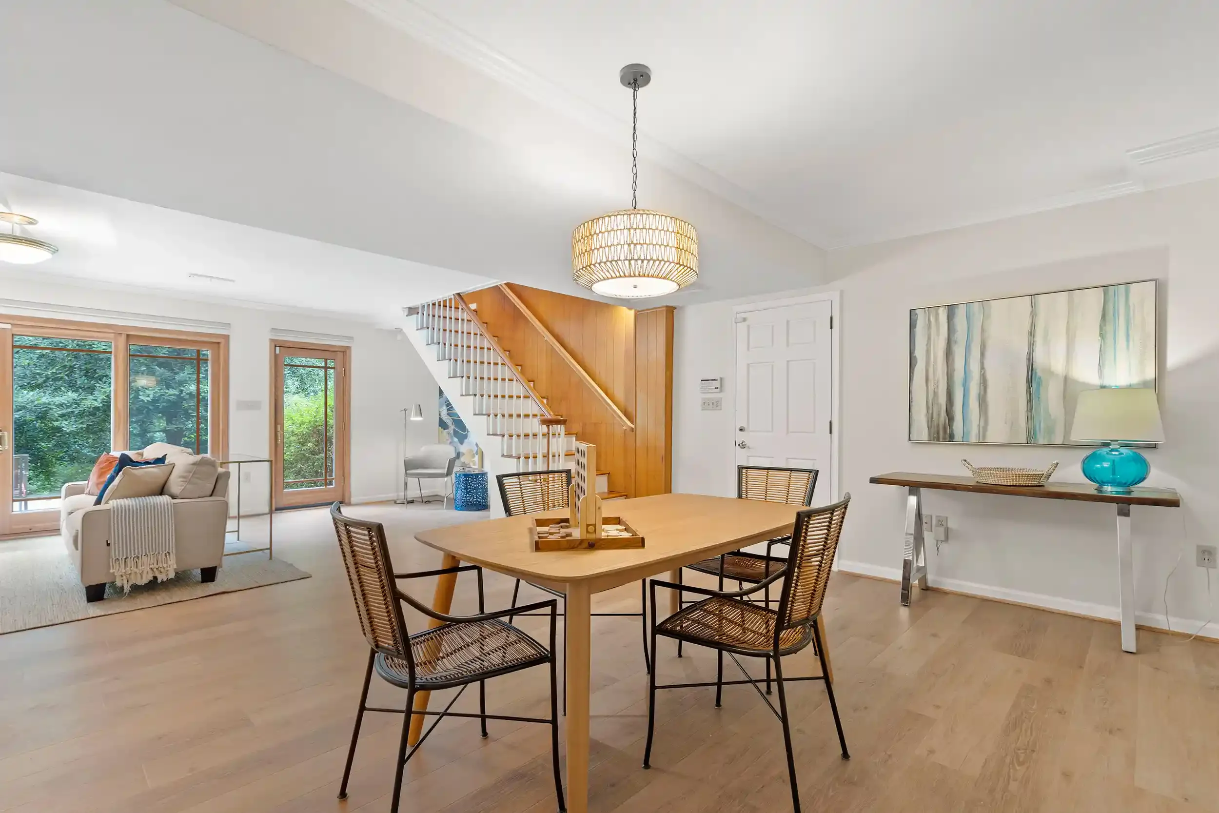 Open-concept living and dining area with large windows, wooden staircase, and modern decor