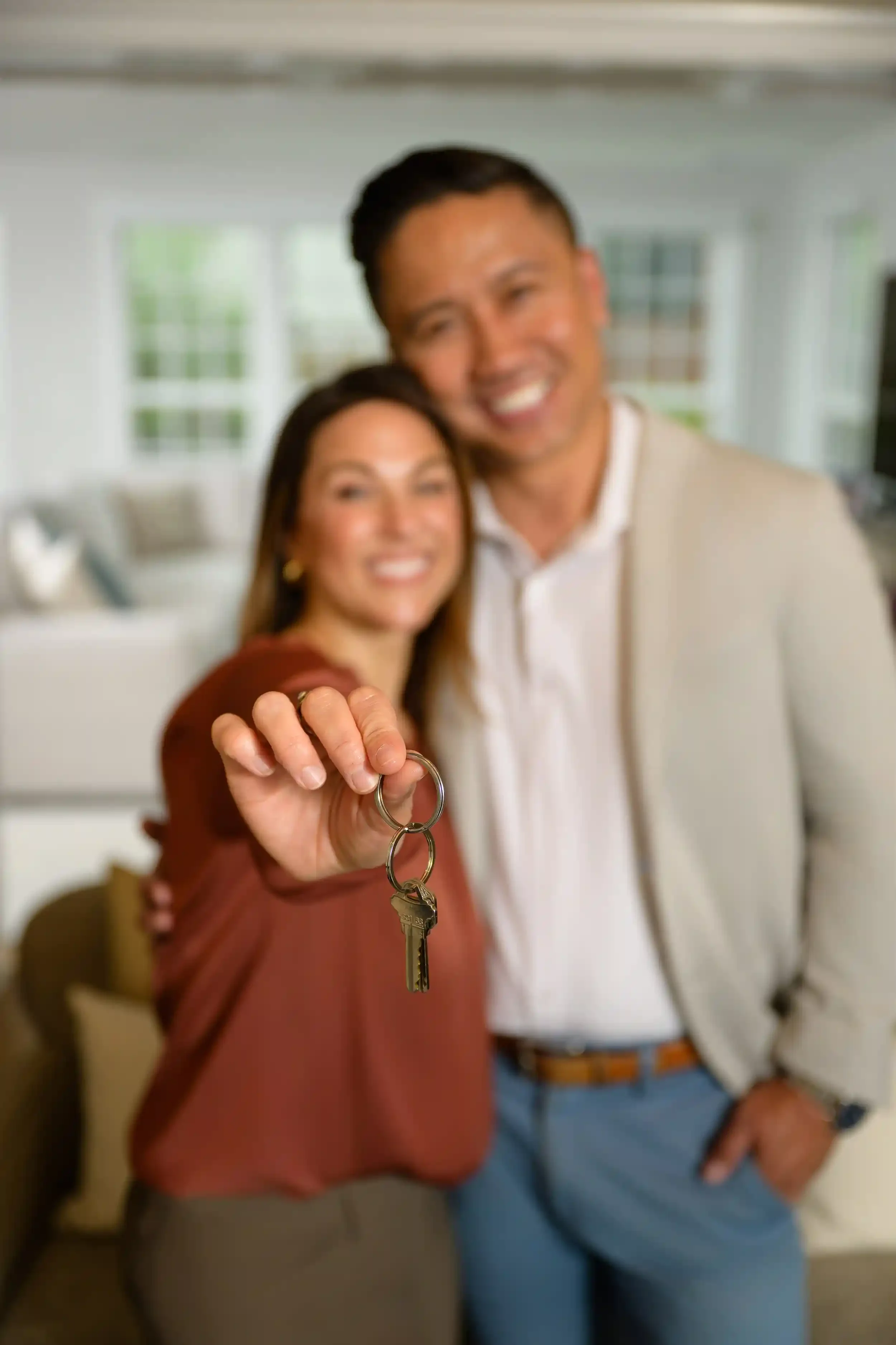 A woman holding up a keyring with a key front and center, with a man standing behind her, smiling in a living room