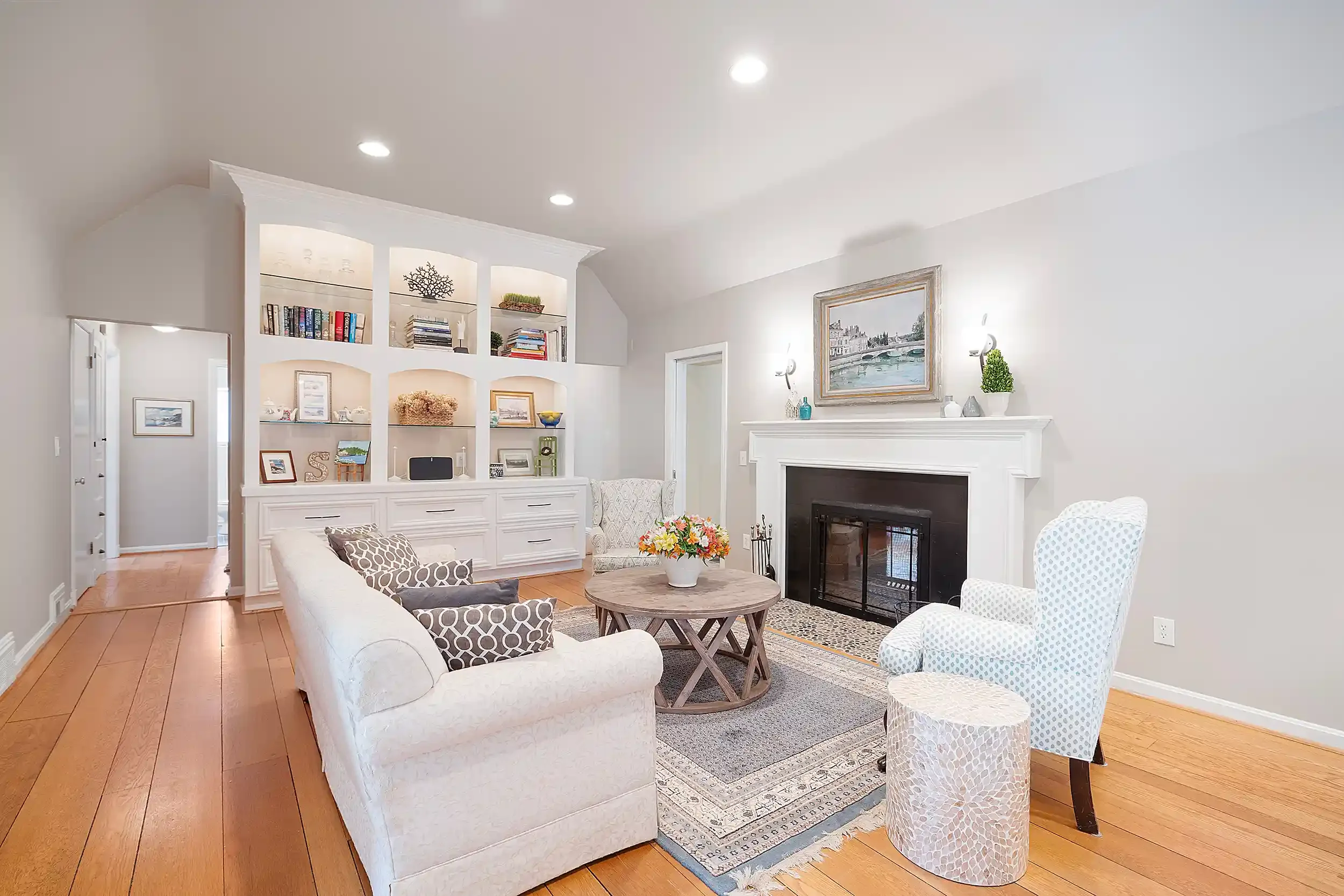 A cozy living room with white walls, hardwood floors, and a white fireplace