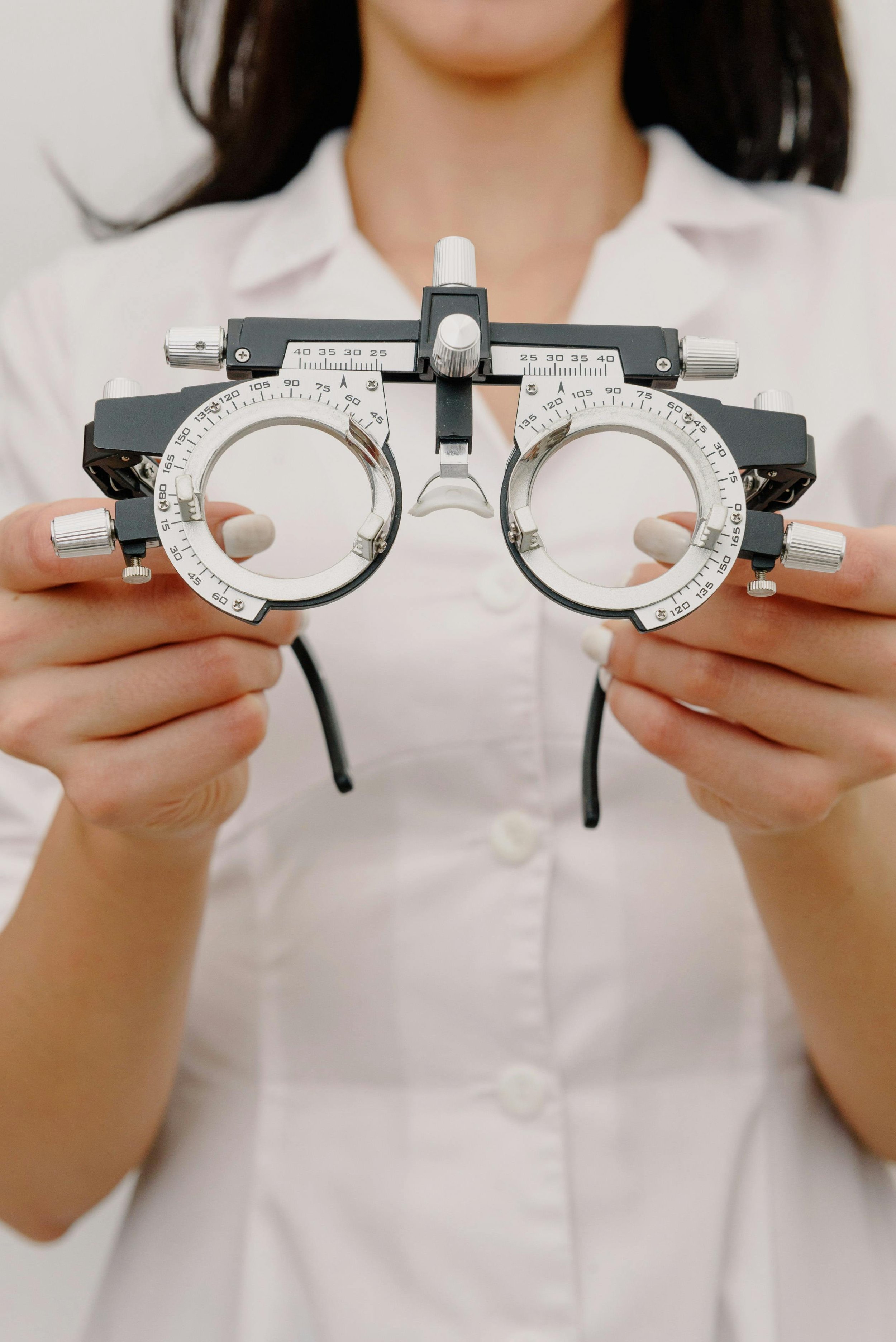 A person wearing a white shirt holding a phoropter eye examination device.