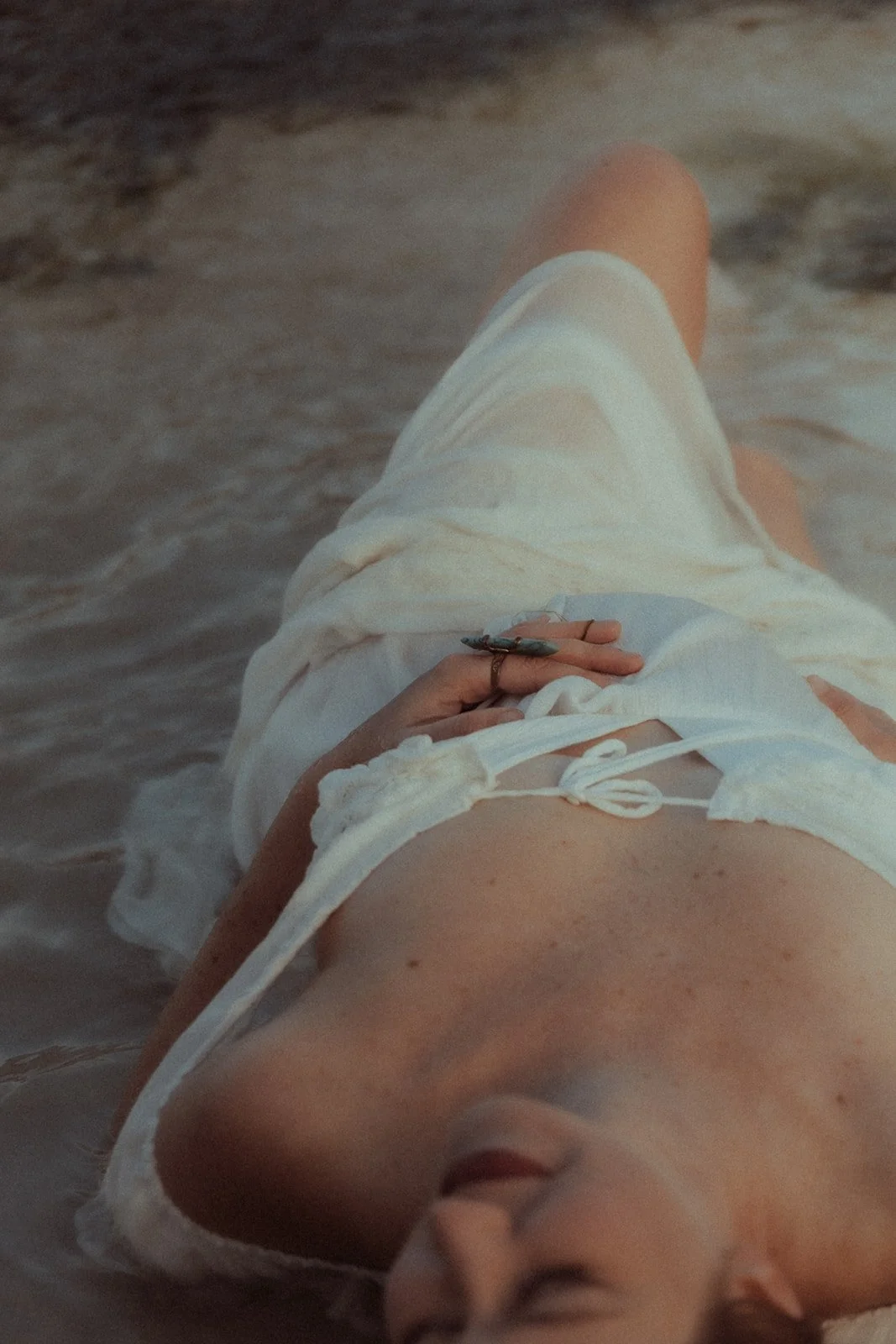 Person lying on a beach in white clothing, holding a small camera.