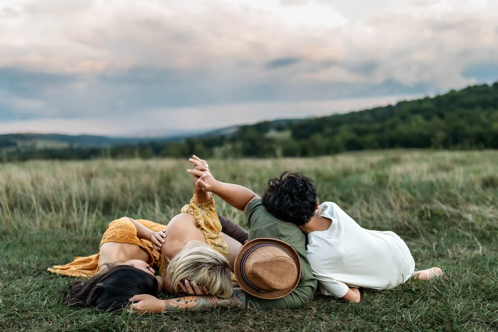 Three young women lying on the grass in a field, resting and relaxing together on a cloudy day.