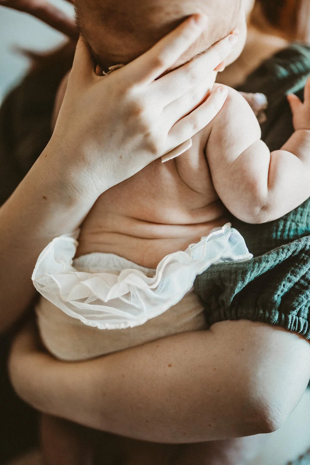 Close-up of an adult holding a newborn baby, with the baby's head resting on the person's hand. The baby is wearing a white, frilly cloth around the waist.
