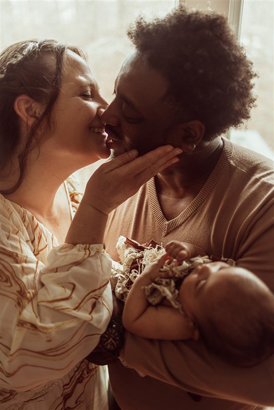 A couple sharing a tender moment with their newborn baby, holding and gently touching the baby's head and face in a cozy indoor setting.