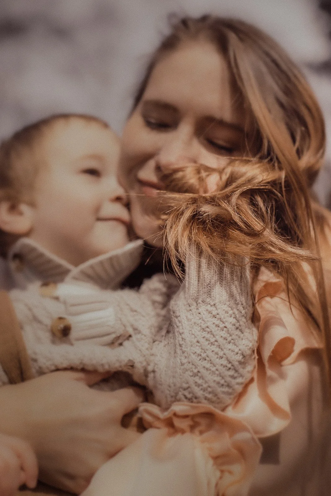 A woman with red hair and a young boy sharing a close embrace, smiling and cuddling.