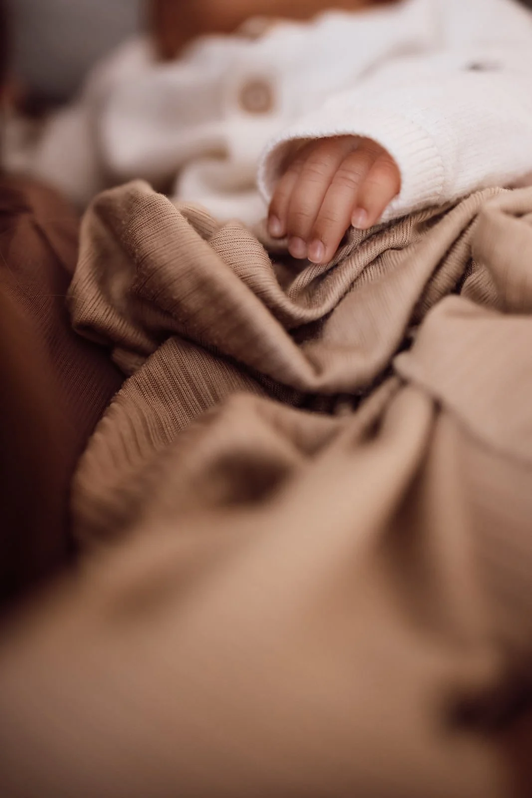 Close-up of a baby's small hand gripping beige and brown clothing fabric.