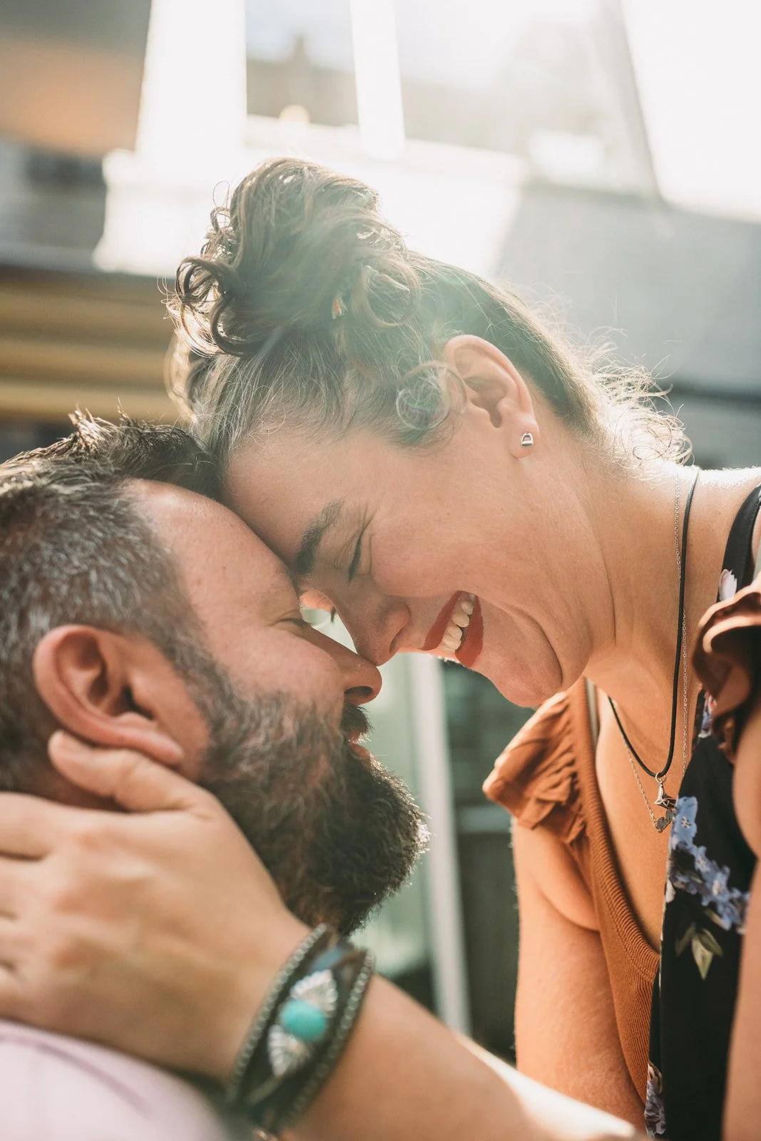 A close-up of a woman and a man with their foreheads touching, smiling and showing affection in a bright, outdoor setting.