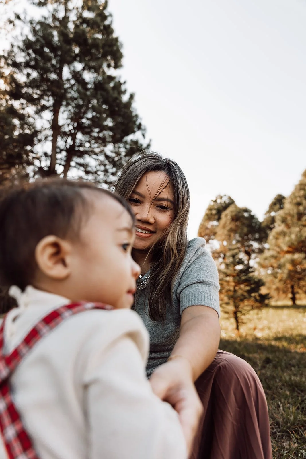 A woman and a young girl sitting outdoors in a park with trees in the background, enjoying a moment together.