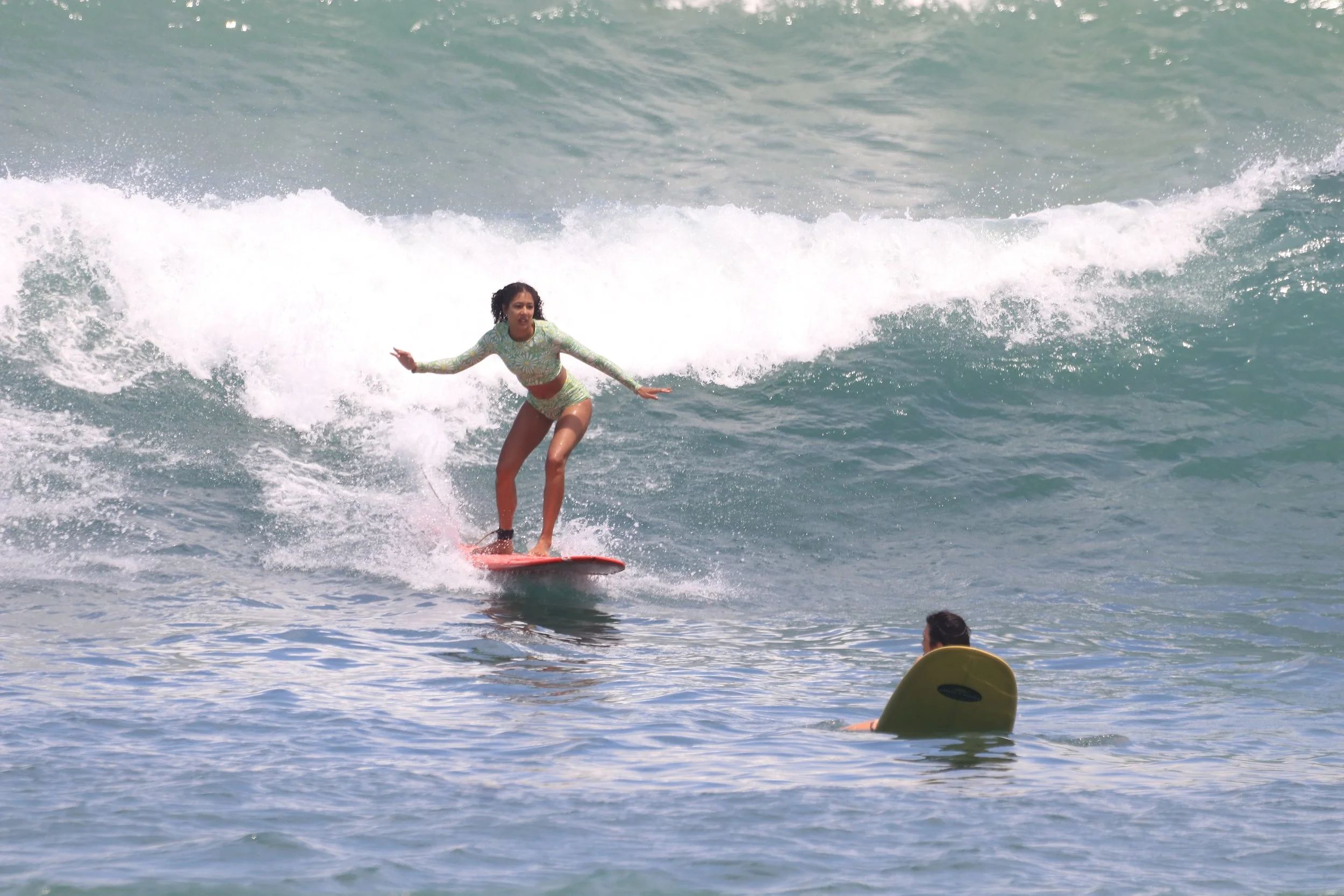 Woman in a floral swimsuit surfing on the ocean with waves in the background.