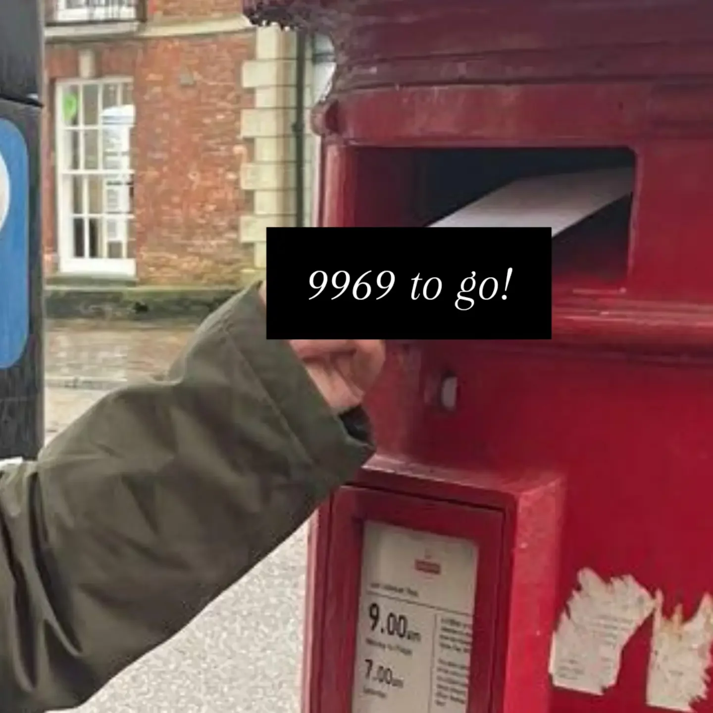 A person is throwing an item into a red donation or collection box labeled with prices. A black overlay with white text reads '9969 to go!'. In the background, brick buildings and a window are visible.