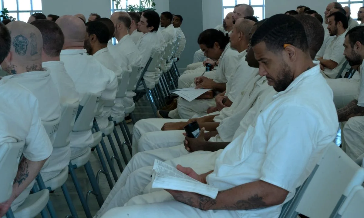 Group of people seated in a class room, all wearing white prison uniforms, attending a Free In My Faith session.