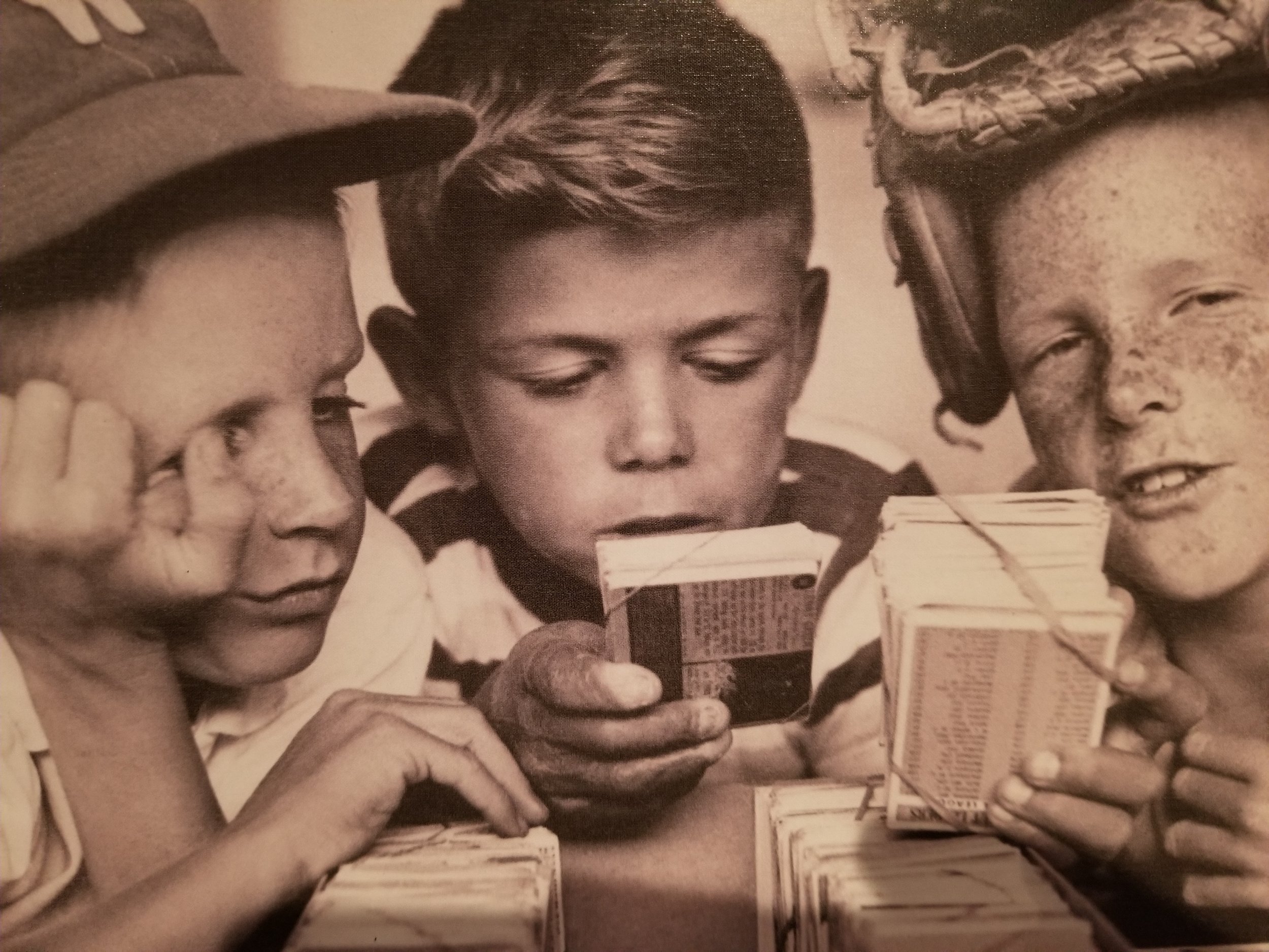 Three young kids in the 1960's examining baseball cards