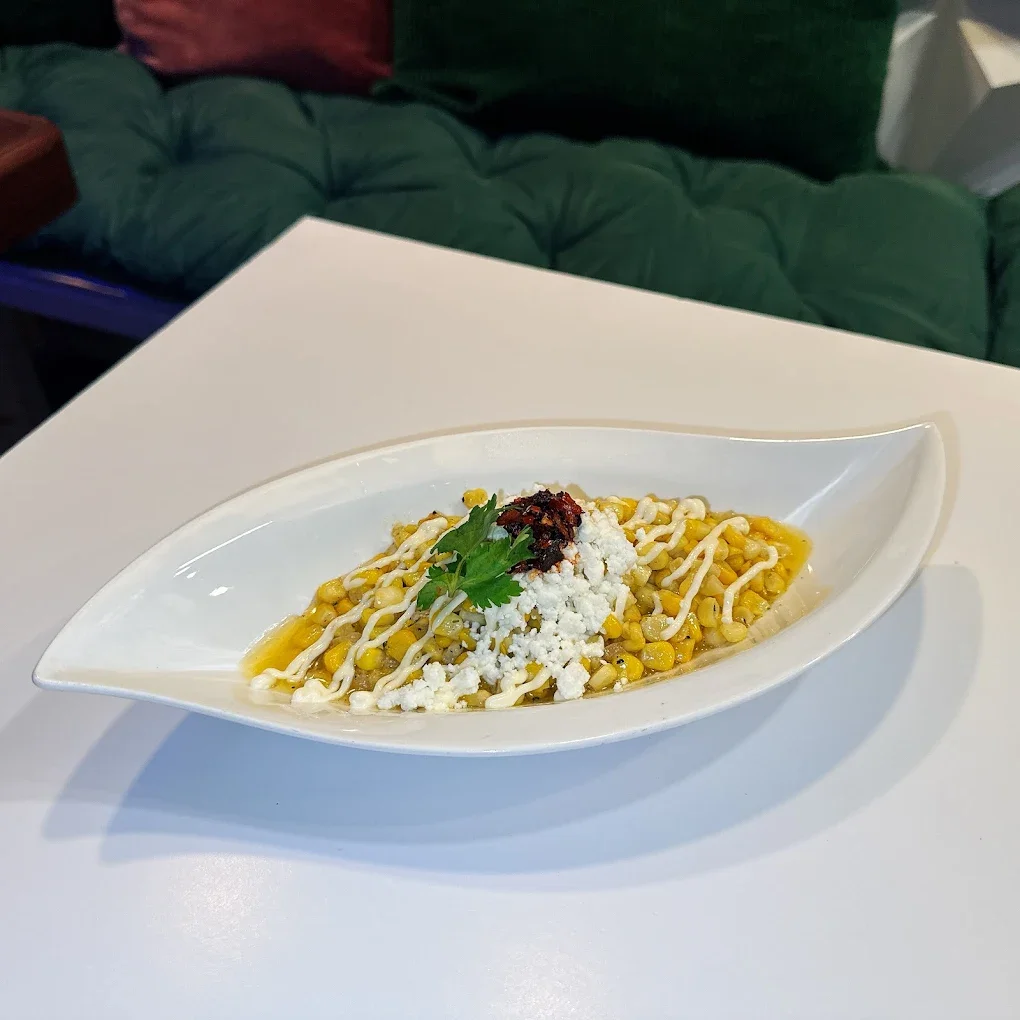Corn salad with crumbled cheese, drizzled mayonnaise, red chili, and cilantro on a white boat-shaped plate.