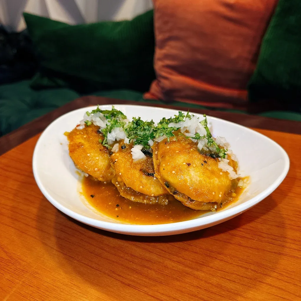 A white bowl of Indian-style curry with potatoes, topped with chopped onions and cilantro, placed on a wooden table.