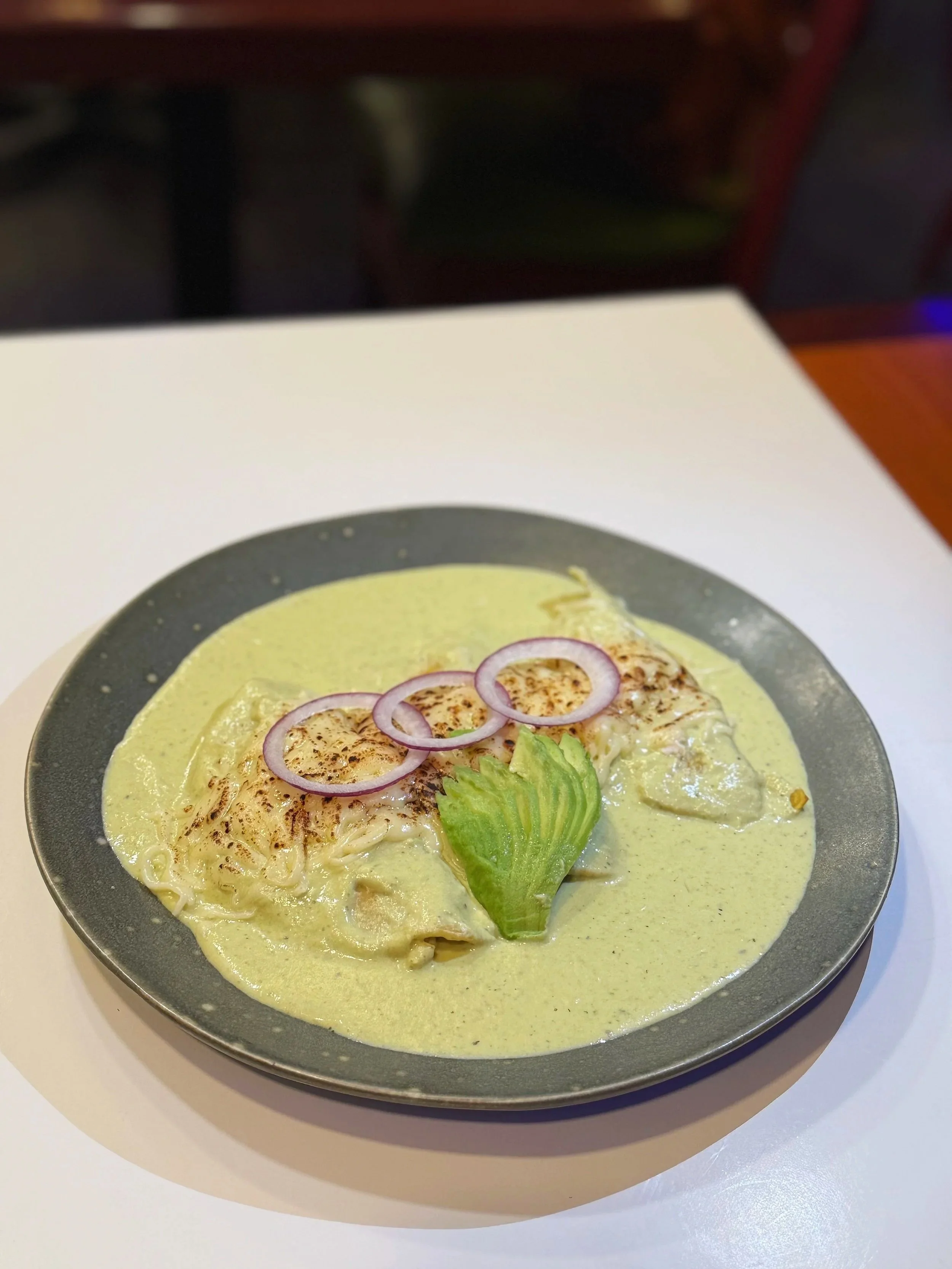 Plate of green curry with chicken, garnished with red onions and a lettuce leaf, on a gray plate.