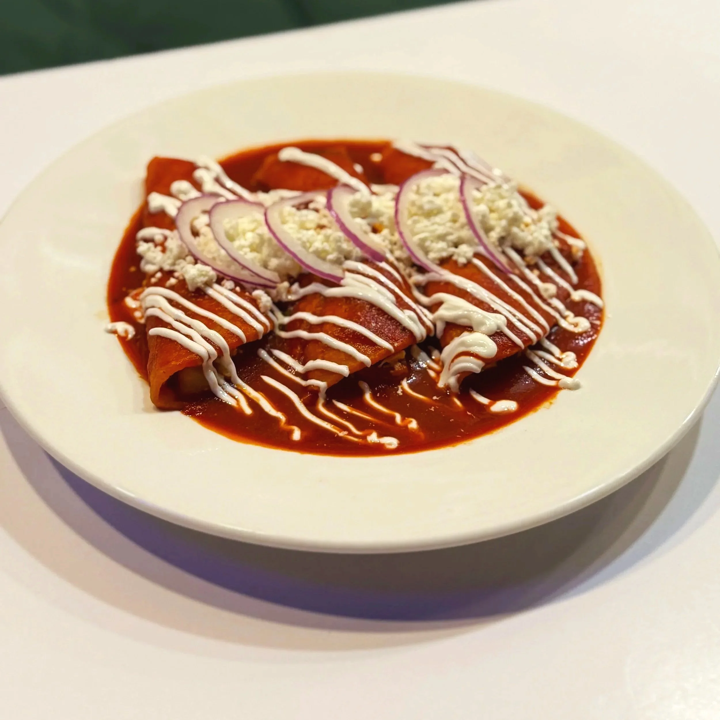 Close-up of a plate with enchiladas topped with sour cream, cheese, and sliced onions, served on a white dish.