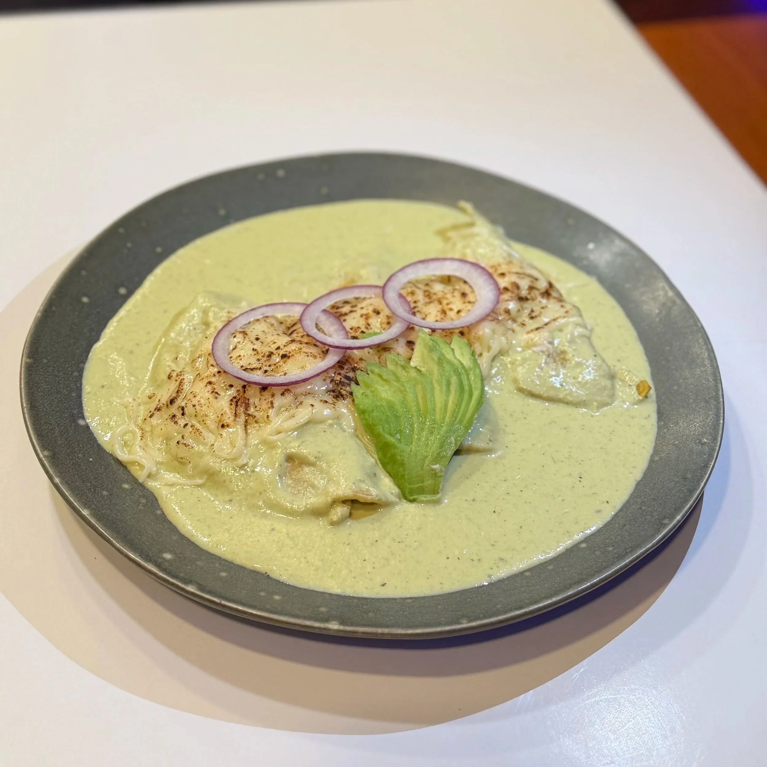 A plate of food with a base of yellow sauce, topped with slices of fish, red onion rings, shredded lettuce, and some spices.