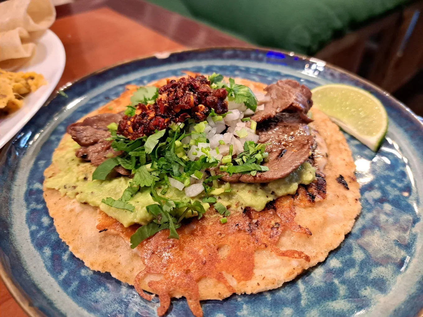 Tacos topped with guacamole, diced onions, cilantro, salsa, and a lime wedge on a blue plate.