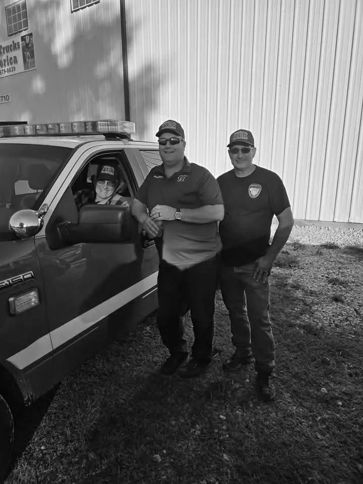 Two police officers and a young man standing next to a police vehicle outside a building.