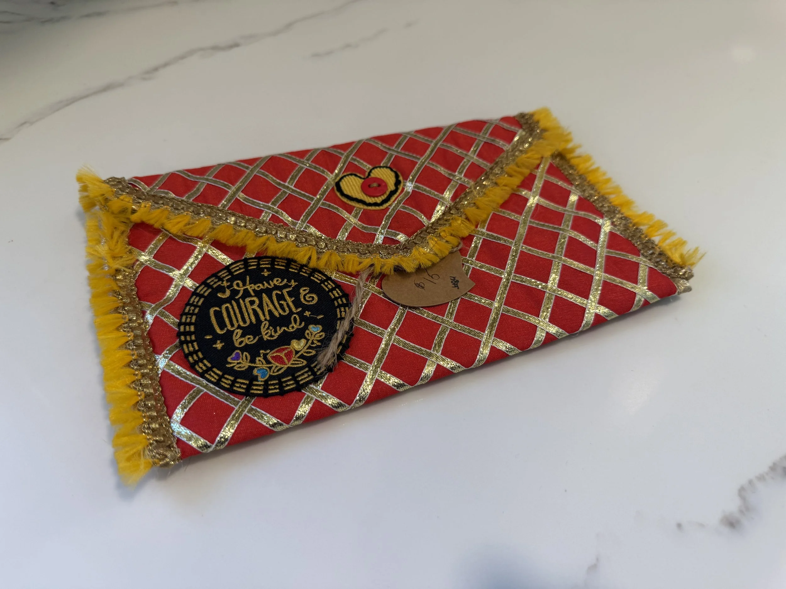 Decorative fabric box with red and gold checkered pattern, yellow fringe, and gold accents, placed on a white surface.