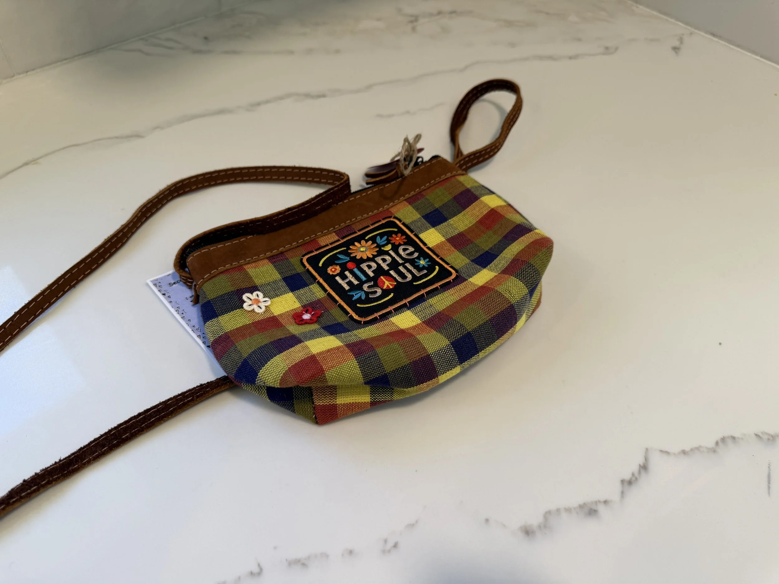 Colorful plaid handbag with a floral patch labeled "Hippie Soul" on a white marble surface.