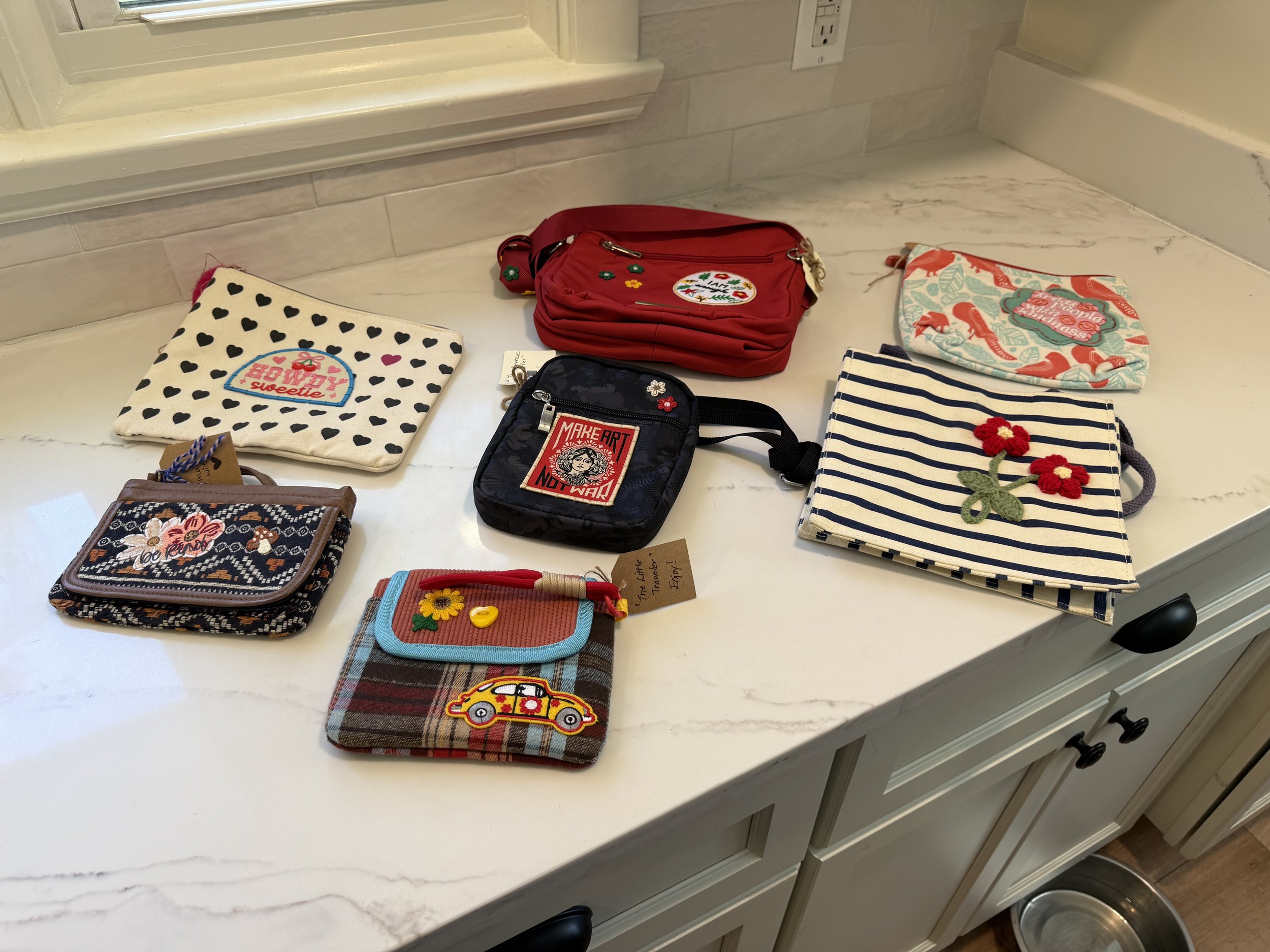 Various small bags and pouches are spread out on a marble countertop, with some featuring colorful designs, patches, or embroidery.