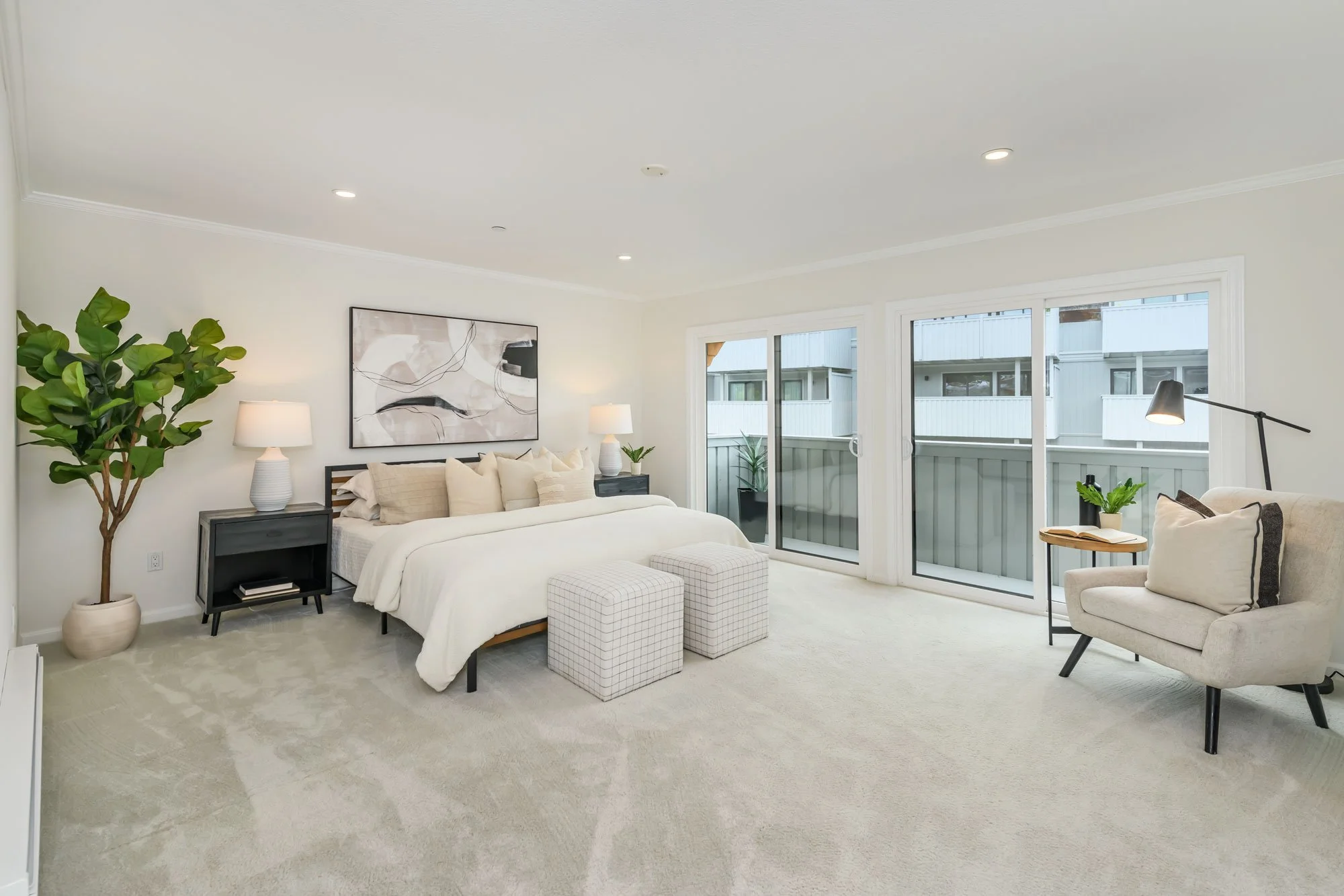 Bright living room with a bed and sitting area, large windows, and minimal modern decor.