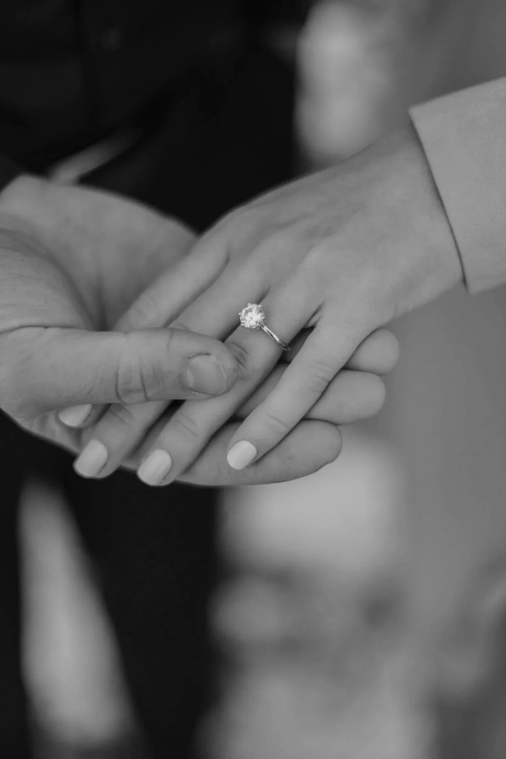 Close-up of two hands, one wearing an engagement ring, clasped together.