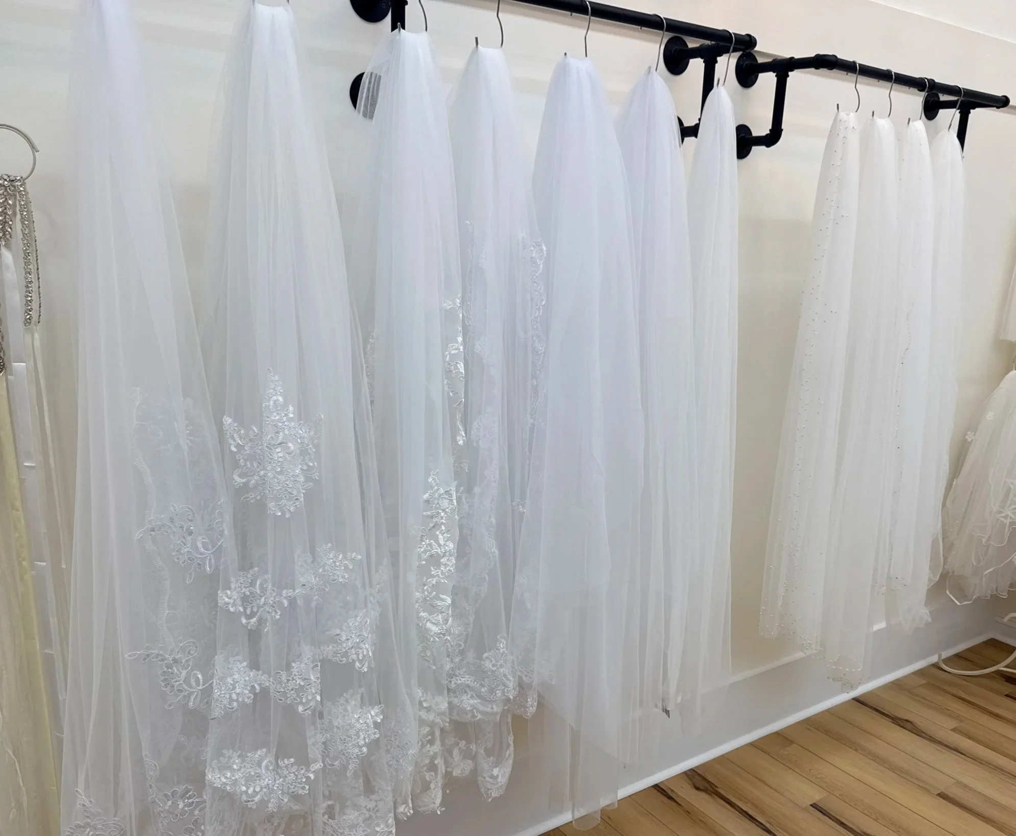 A row of white wedding veils hanging on black hooks against a white wall.