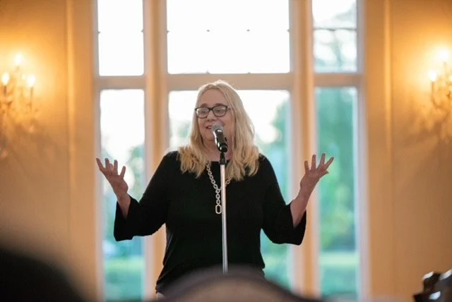 Dreama speaking into a microphone during a live presentation, engaging an audience with an interactive and inspiring talk.