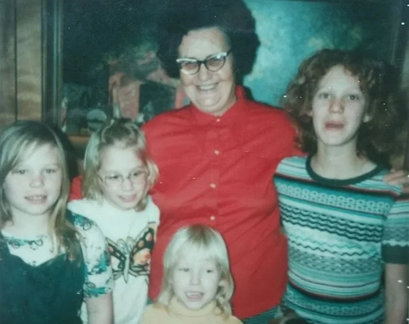 An older woman smiling with a group of young girls during a community gathering, reflecting her commitment to connection, mentorship, and personal growth.